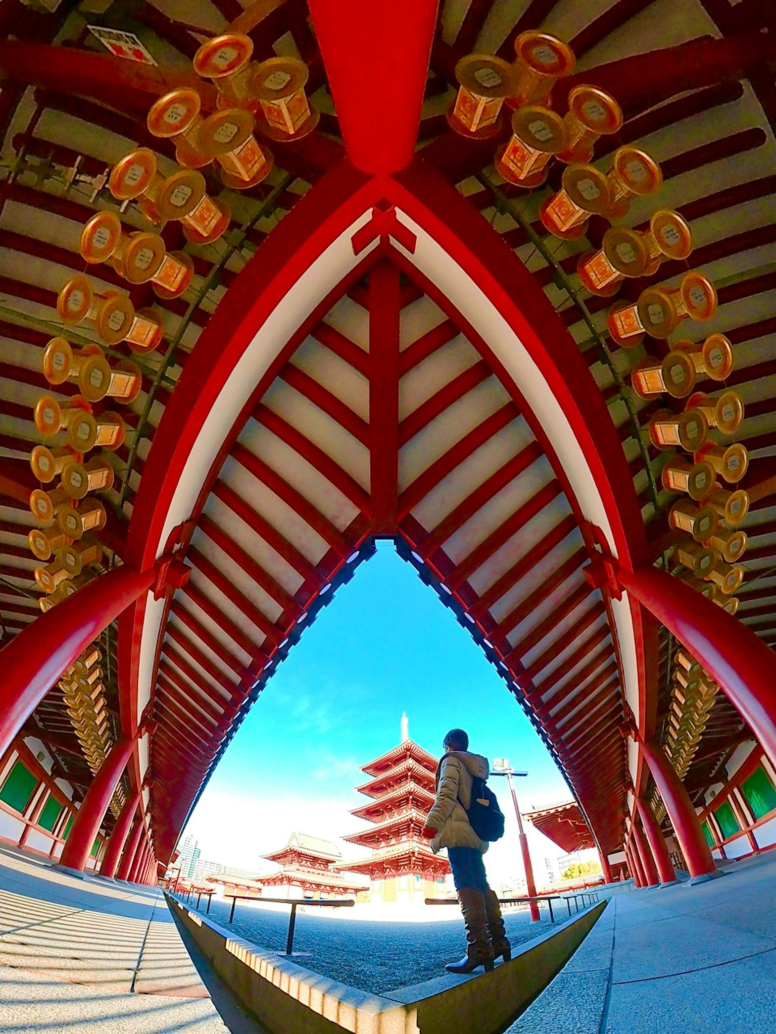 Une personne se tenant sous une arche avec un toit rouge et de grandes lanternes dans un temple