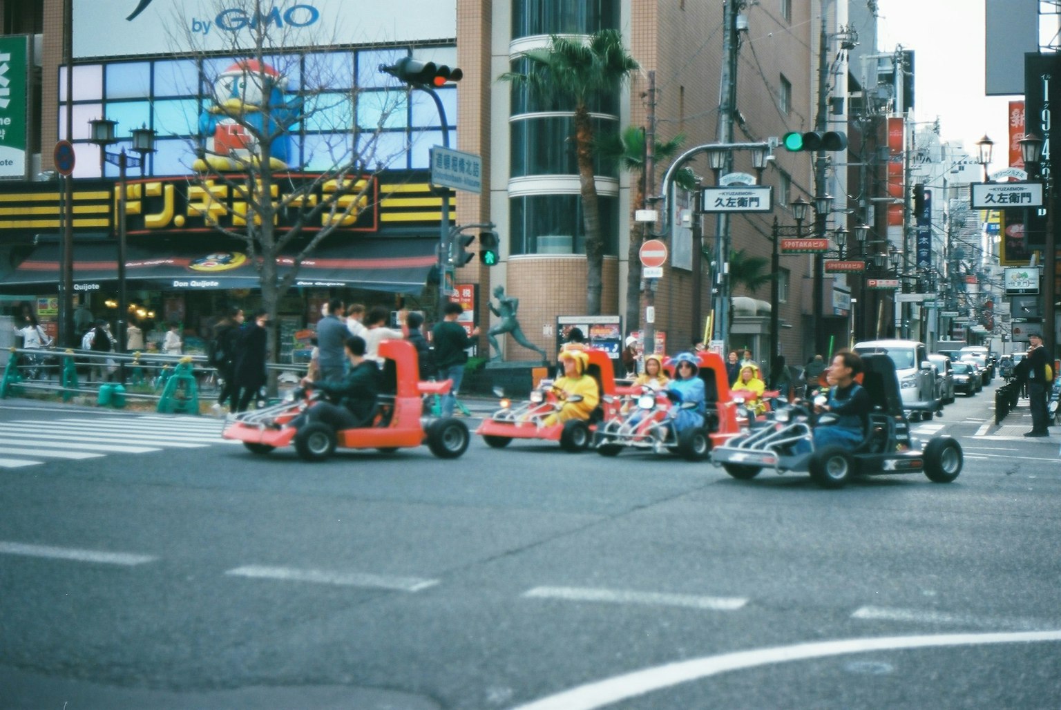 Escena de personas conduciendo go-karts en una intersección con edificios comerciales