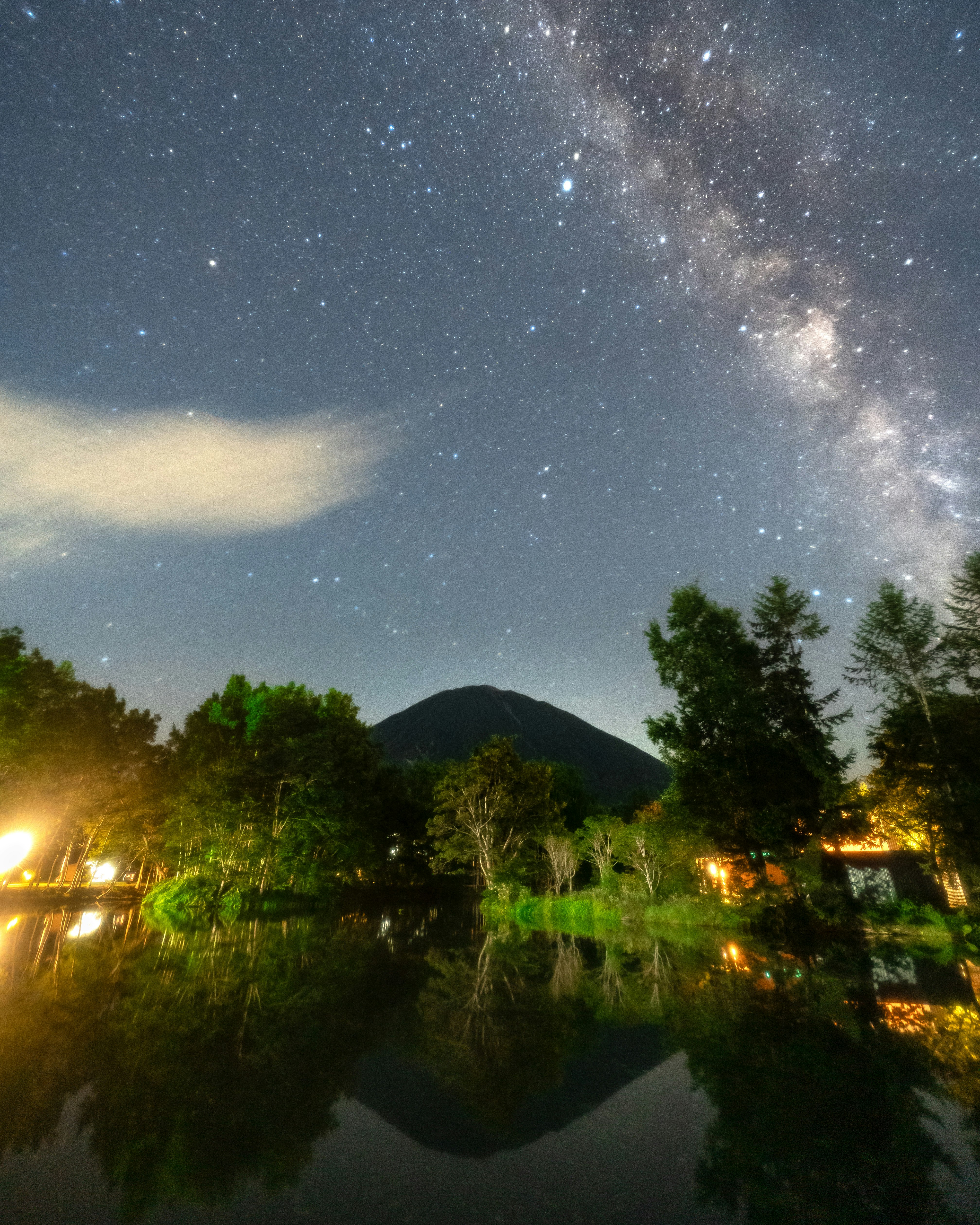 夜空に広がる天の川と湖畔の木々と灯り