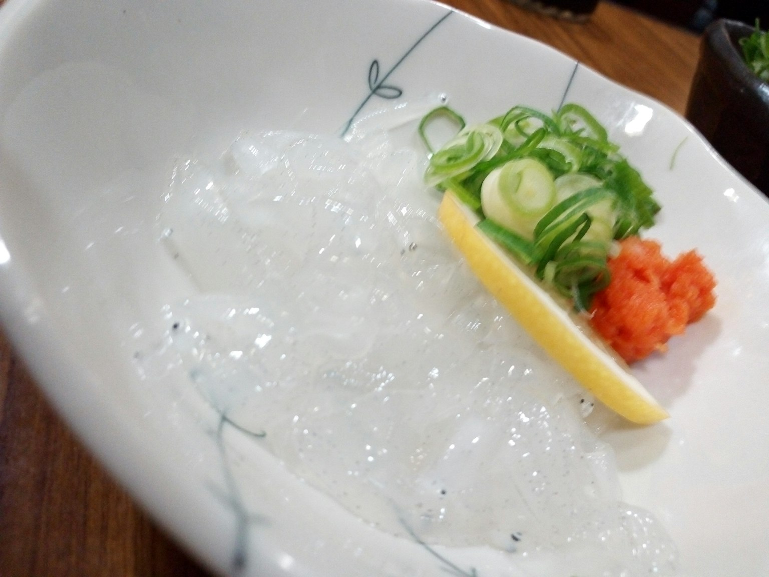 Sashimi trong suốt với hành lá băm nhỏ và một lát chanh kèm theo wasabi