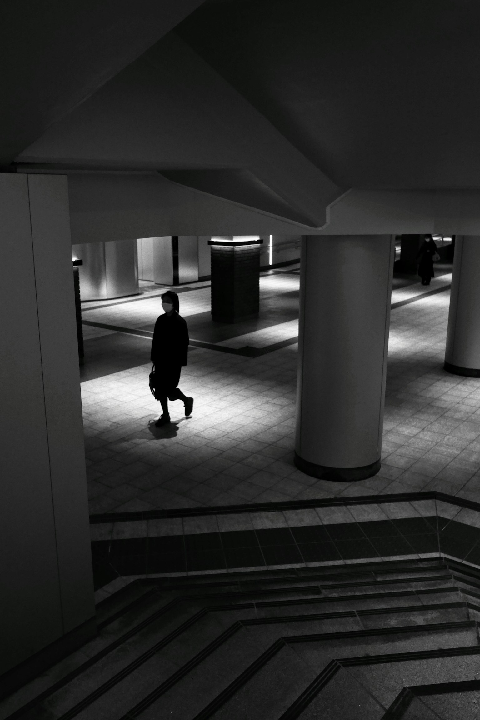 Silhouette of a person walking in a dimly lit space with architectural columns