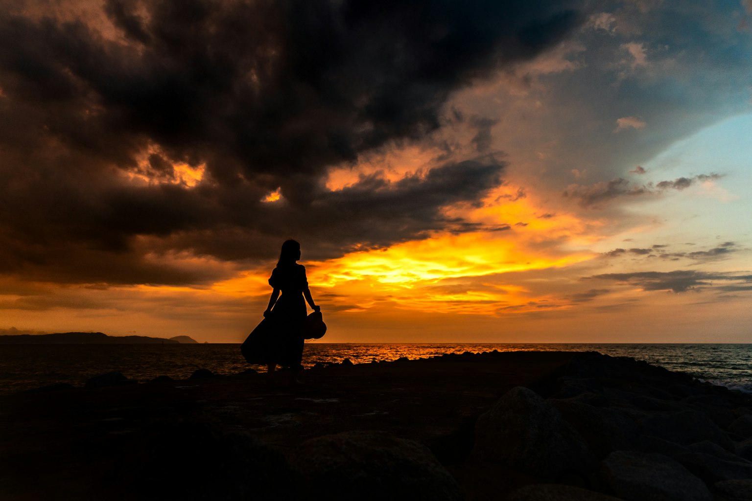 Silhouette of a person standing on the coast against a sunset