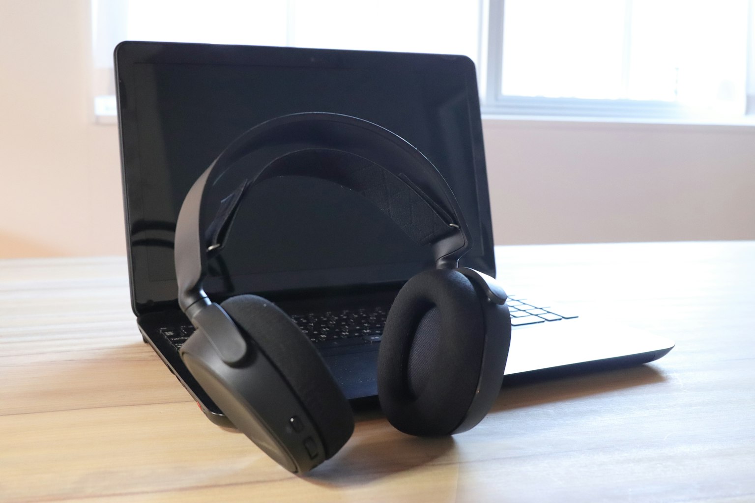 Tai nghe đen đặt trước laptop trên bàn gỗ