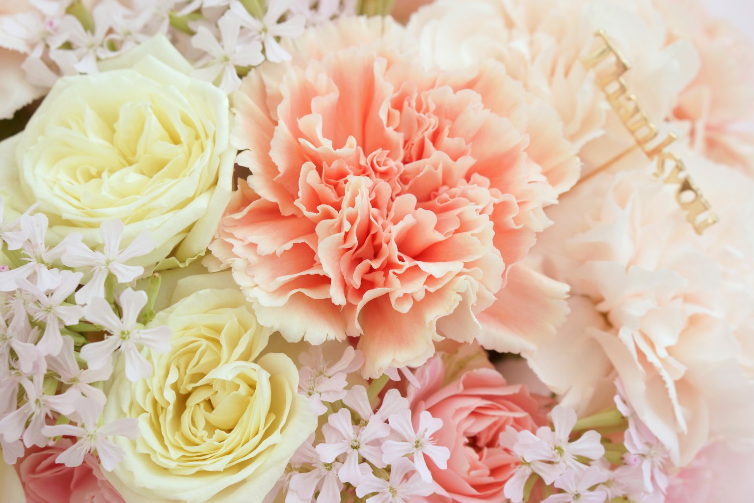 Gros plan d'un bouquet avec des fleurs aux couleurs douces incluant des roses blanches et des œillets pêches