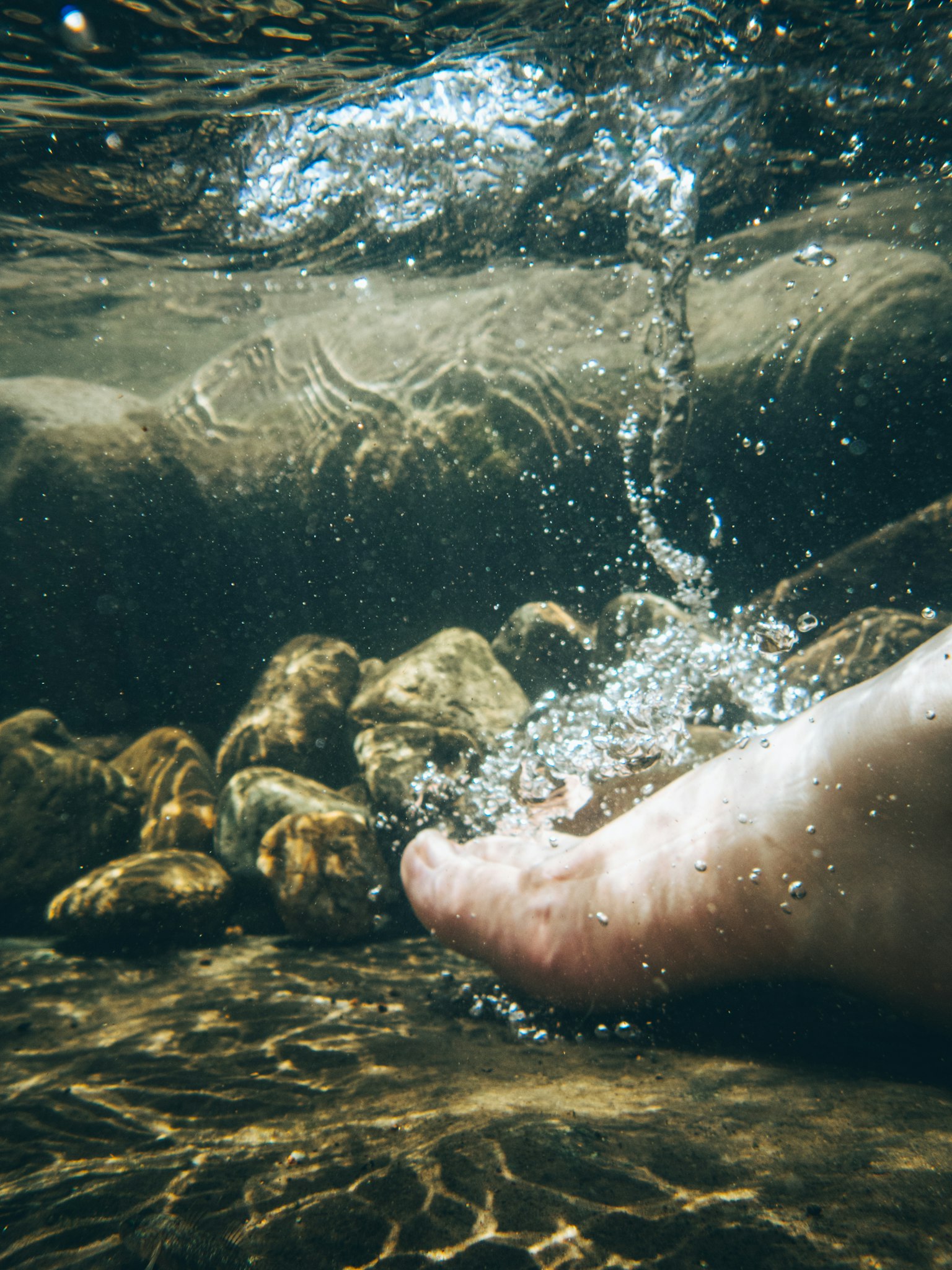 Piede nudo immerso nell'acqua con pietre e bolle