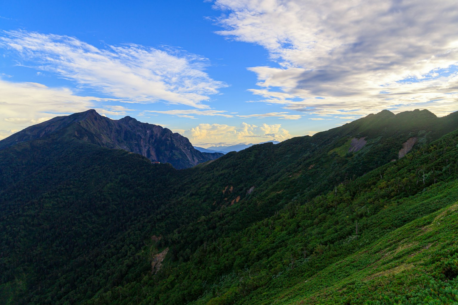 Hermosa paisaje montañoso con cielo azul y nubes colinas verdes y picos distantes