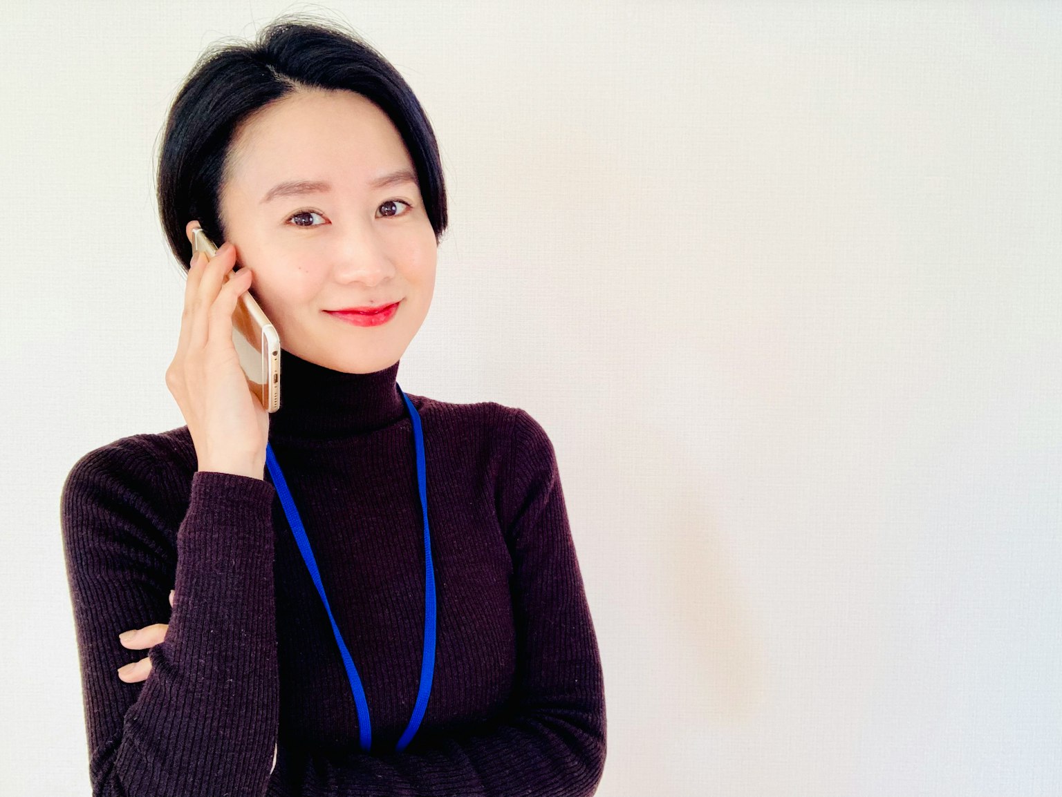 正在打电话的女性肖像，穿着黑色高领衫，佩戴蓝色挂绳，面带自信微笑