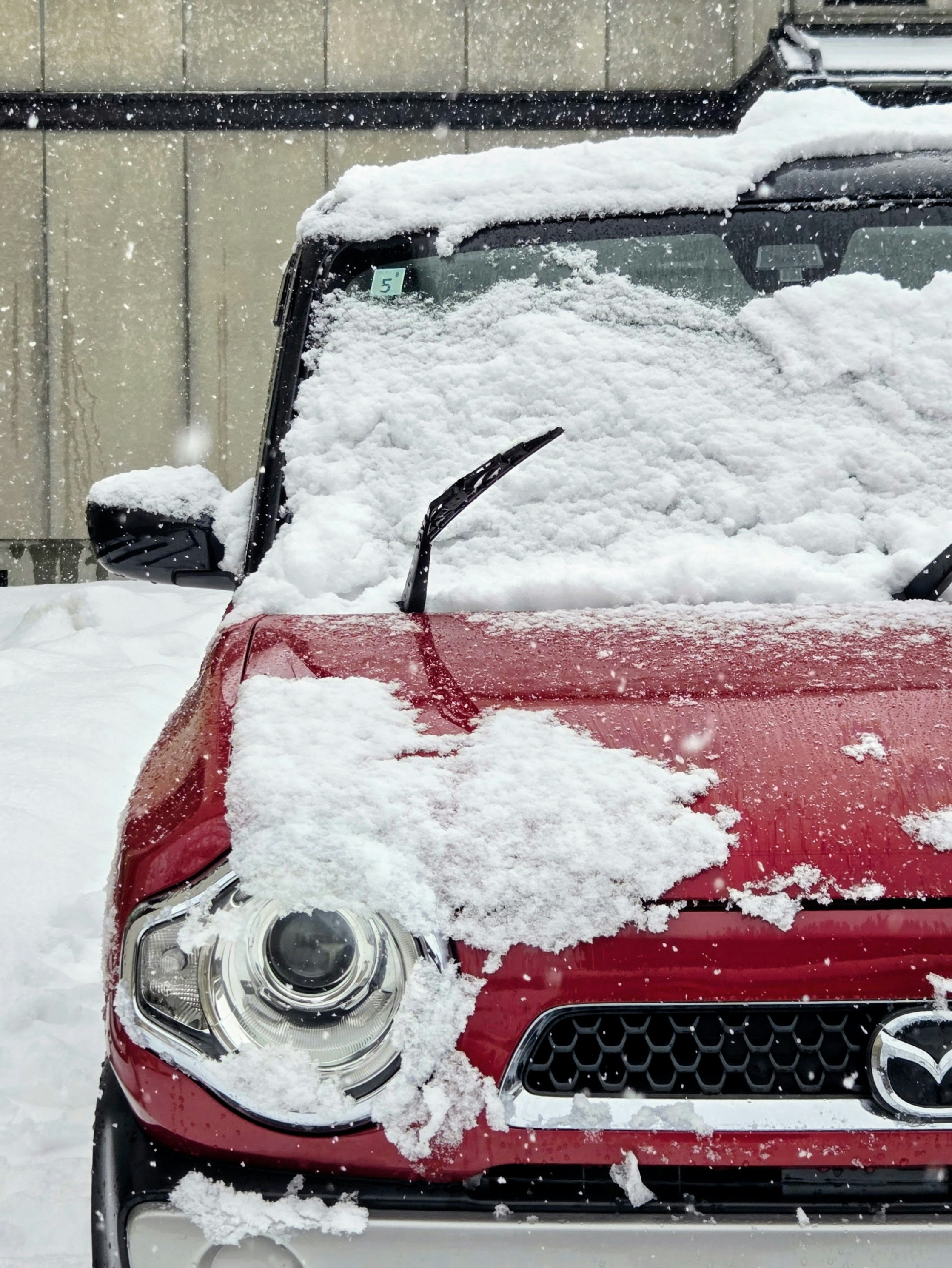 雪に覆われた赤い車の前景 車のヘッドライトとワイパーが見える