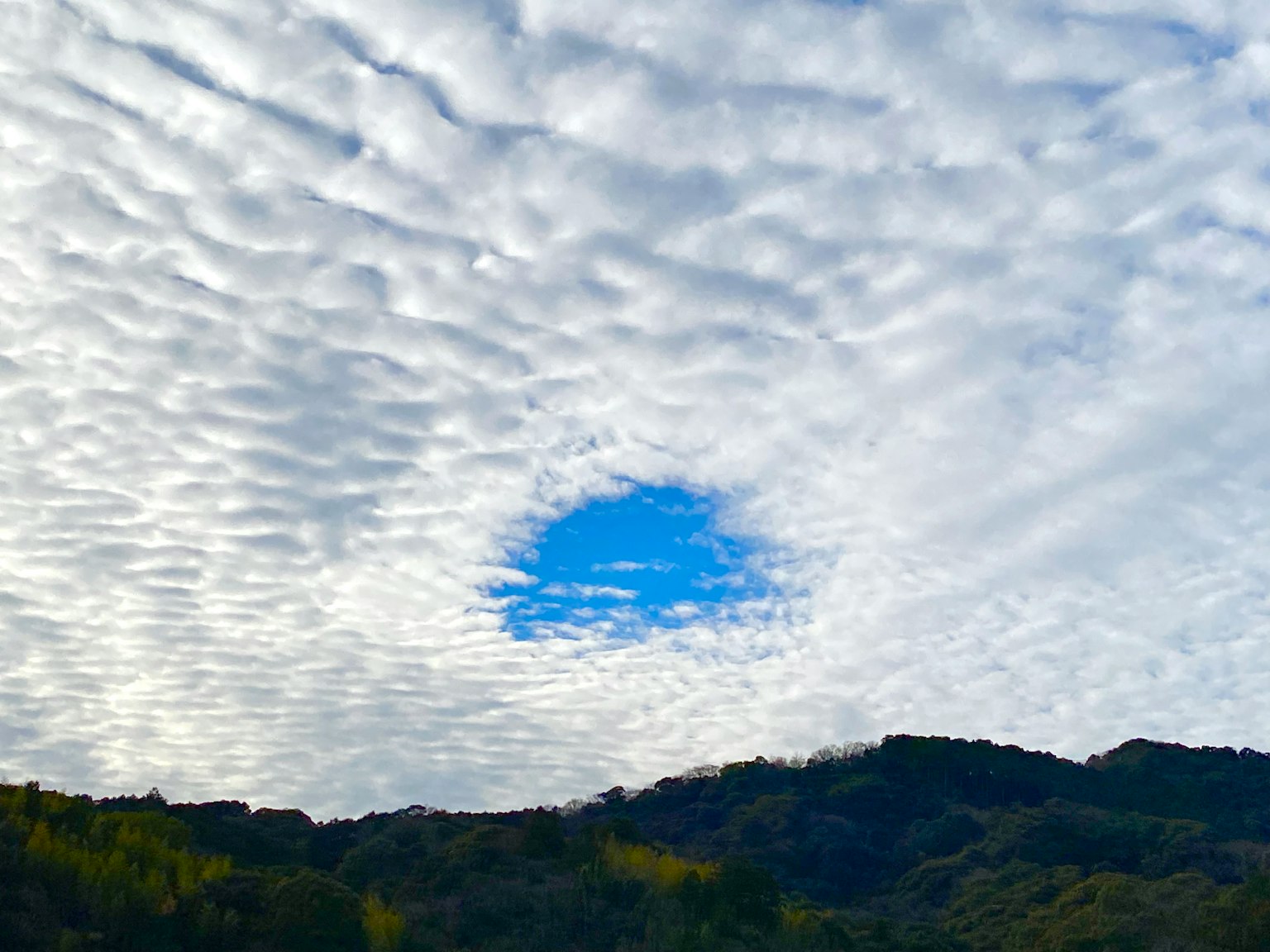 Cielo con un buco nelle nuvole che rivela il blu e montagne sottostanti