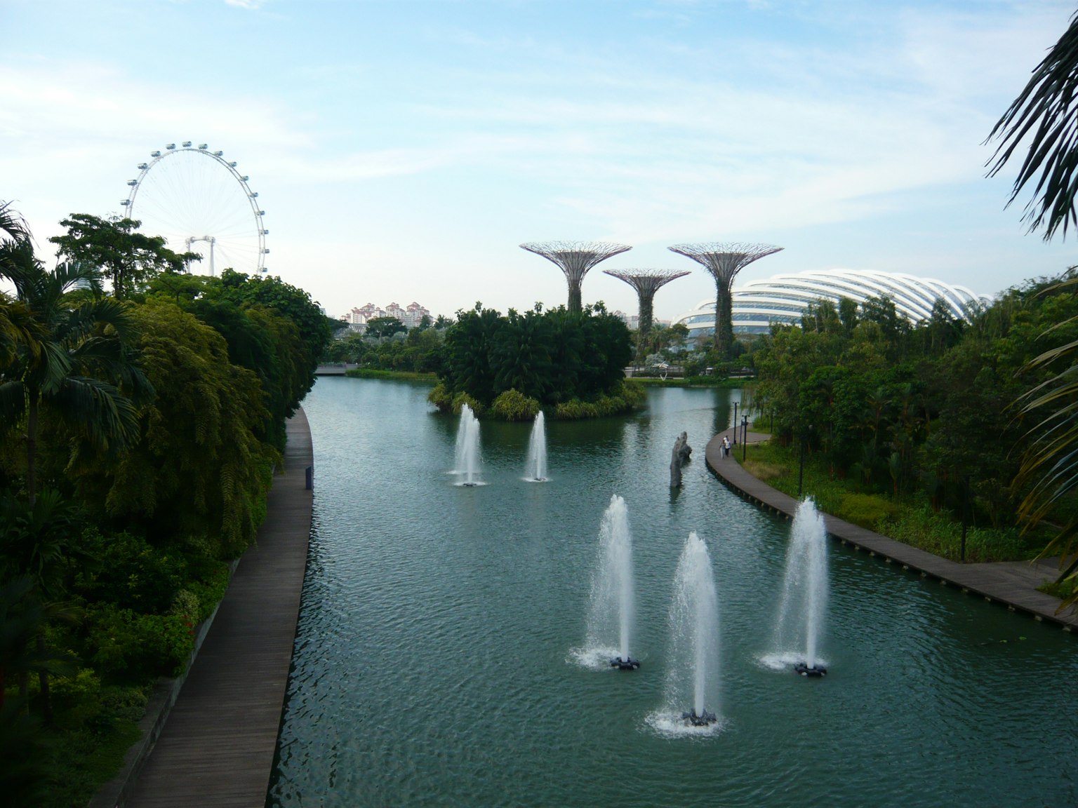 Scenic park view with fountains lined up along the water and a Ferris wheel in the background