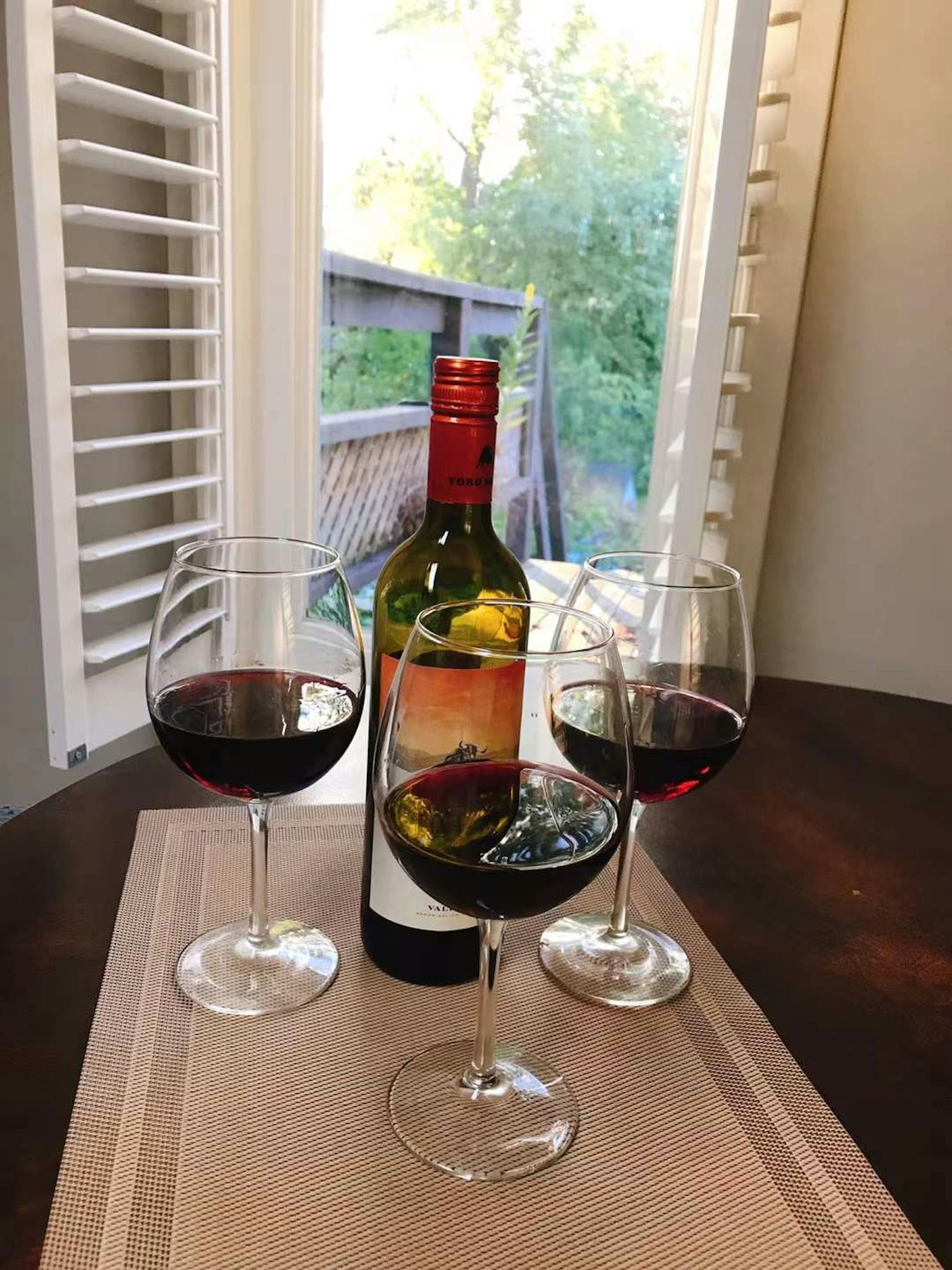 一瓶红酒和三只酒杯放在桌子上，窗外有自然光