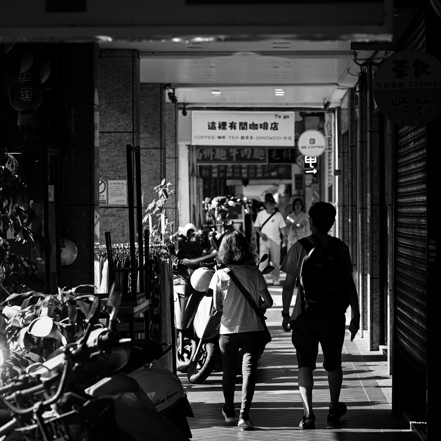 人們走在單色街景中，旁邊停著自行車和摩托車