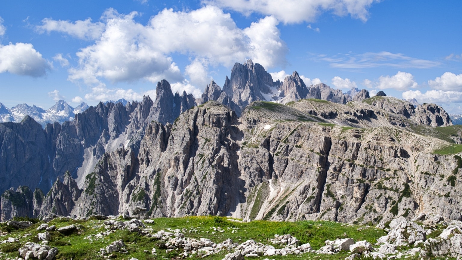 Beeindruckende Gebirgskette mit blauem Himmel grünem Wiesengelände und Felsformationen