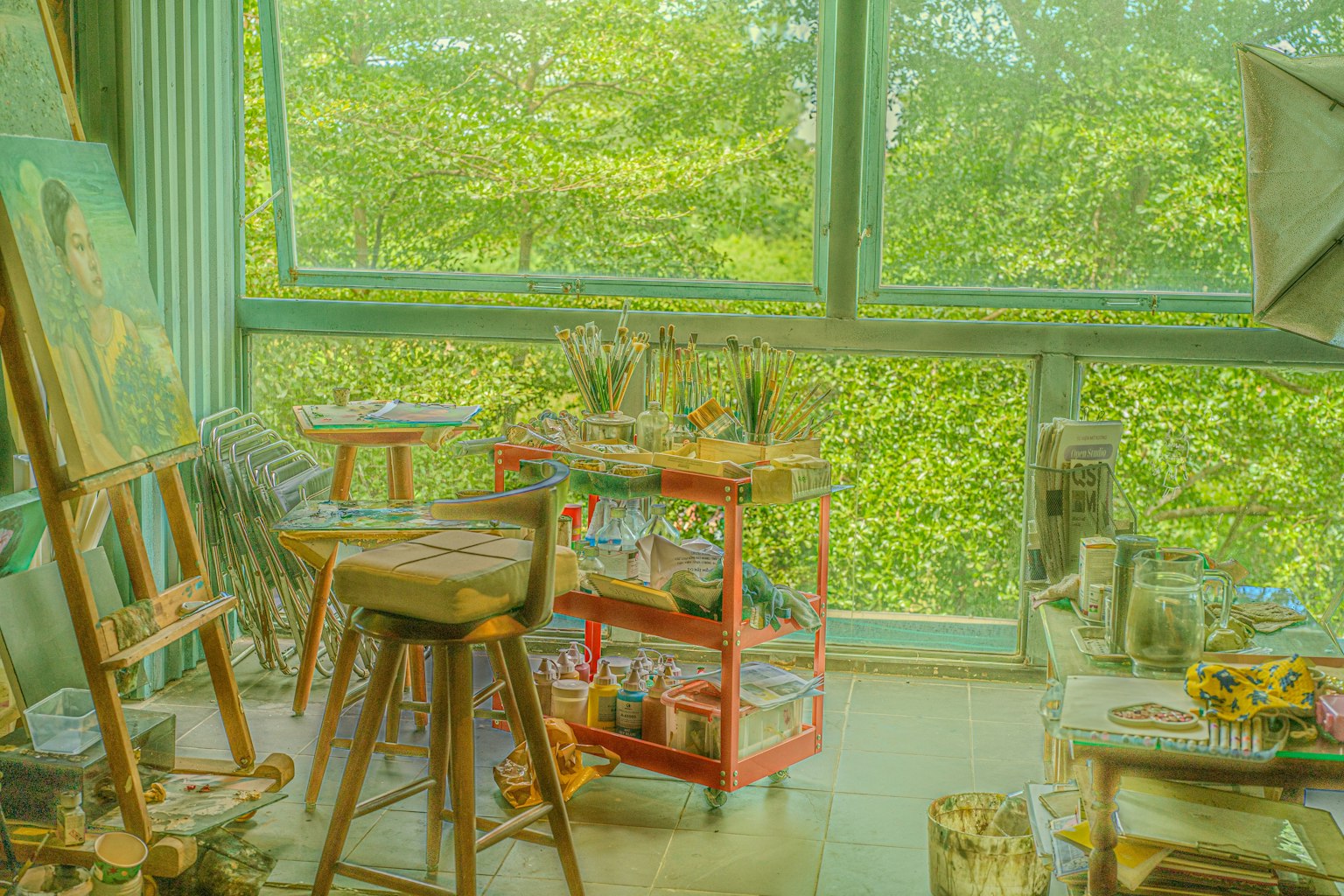 明るいアトリエの内部 緑の景色が見える大きな窓 絵画用のイーゼルと道具が並ぶ