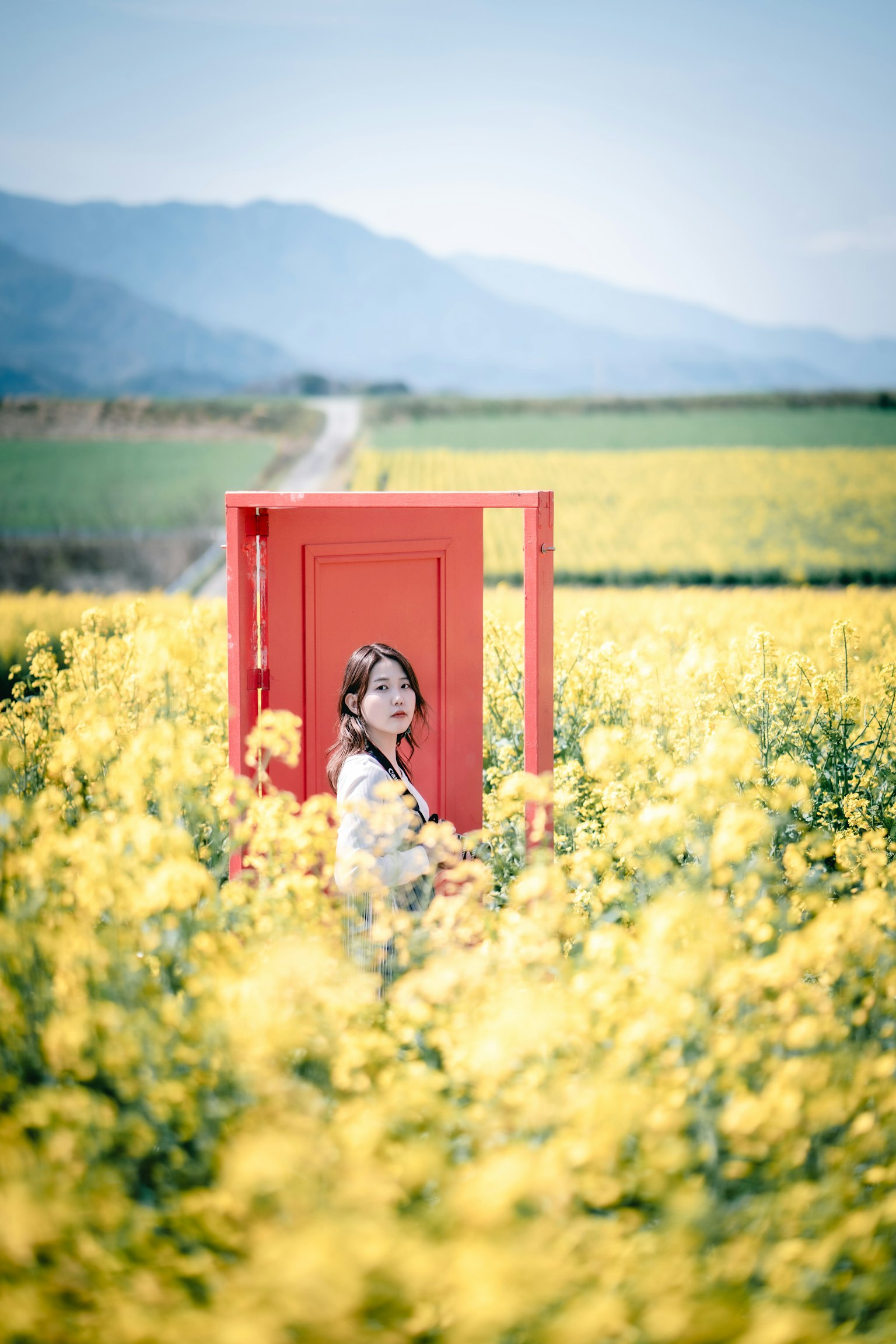 Una mujer de pie en un campo de flores amarillas con una puerta roja