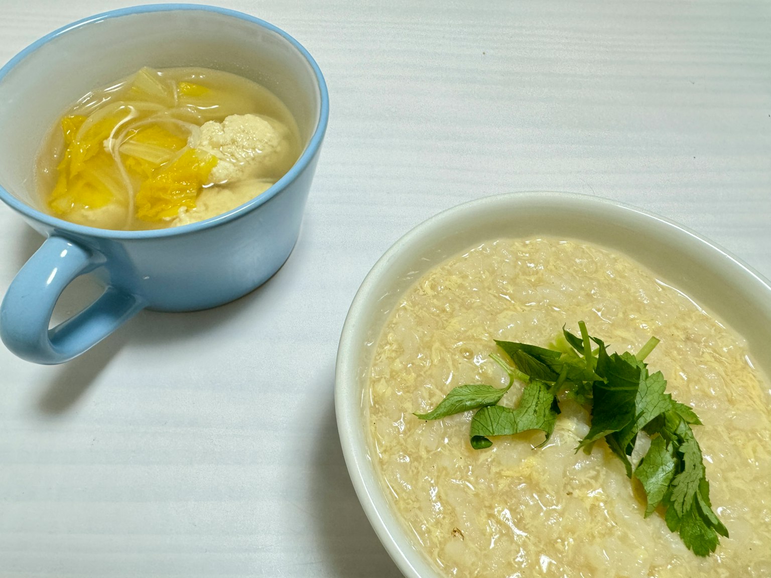 Bubur krim dalam mangkuk putih dengan sup dalam cangkir biru