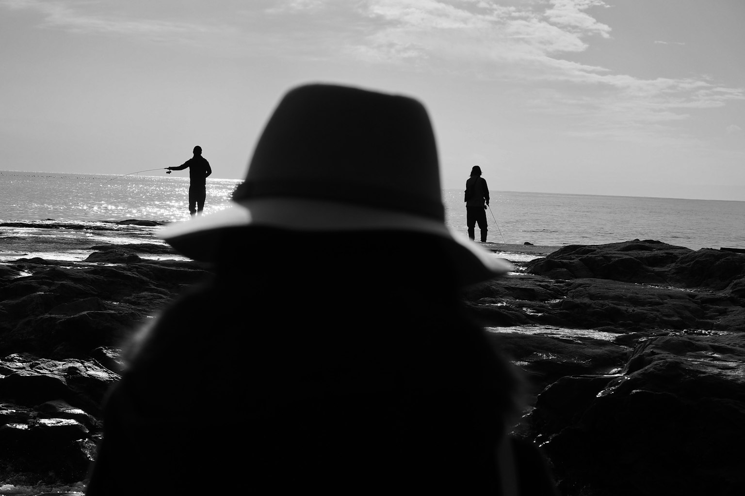 Silhouette einer Person mit Hut am Strand mit zwei weiteren Figuren im Hintergrund