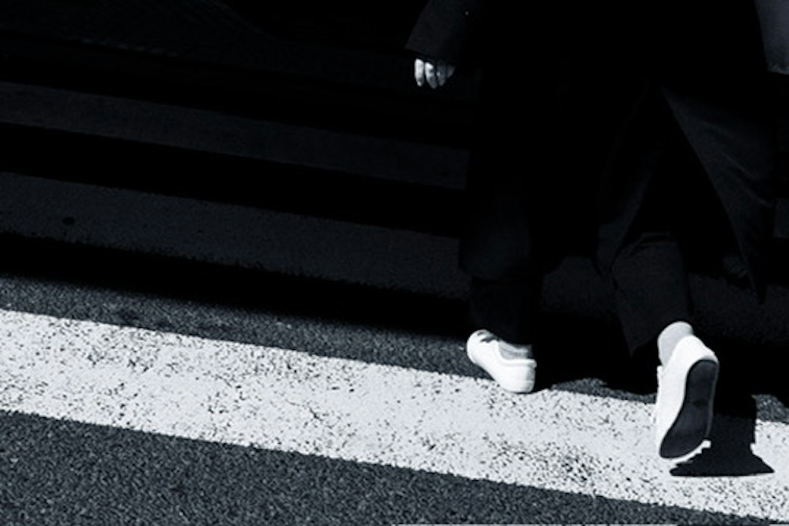 Un pied in sneakers bianche che cammina su un attraversamento pedonale con sfondo scuro