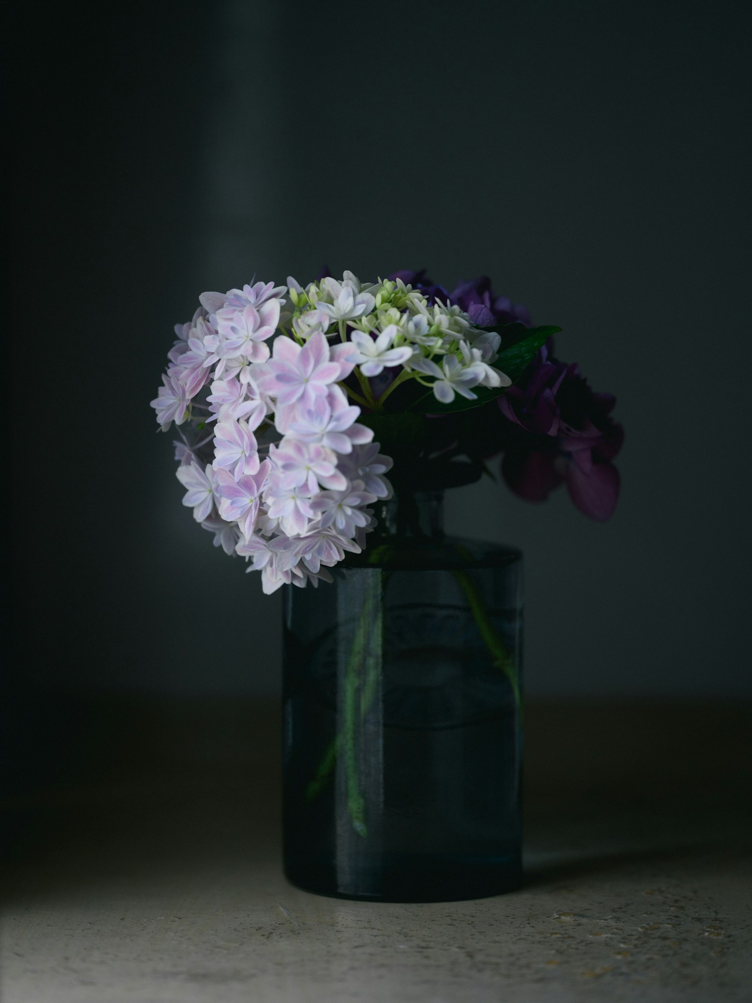 Un bouquet de fleurs violettes et blanches dans un vase sombre sur un fond tamisé