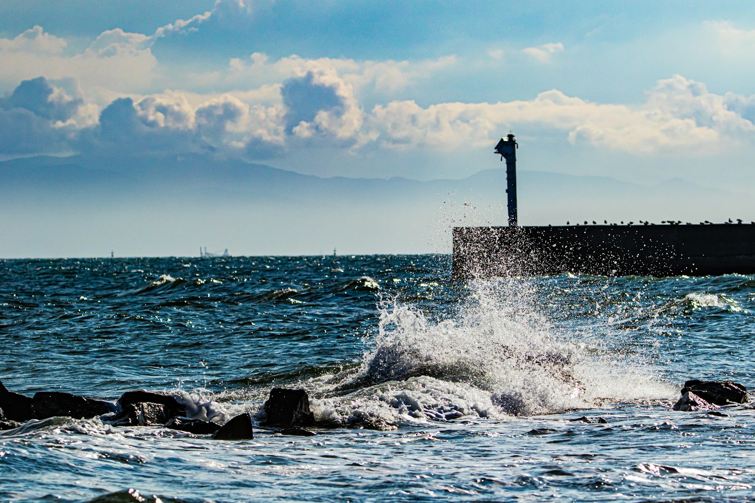 Seascape with crashing waves and lighthouse in the distance