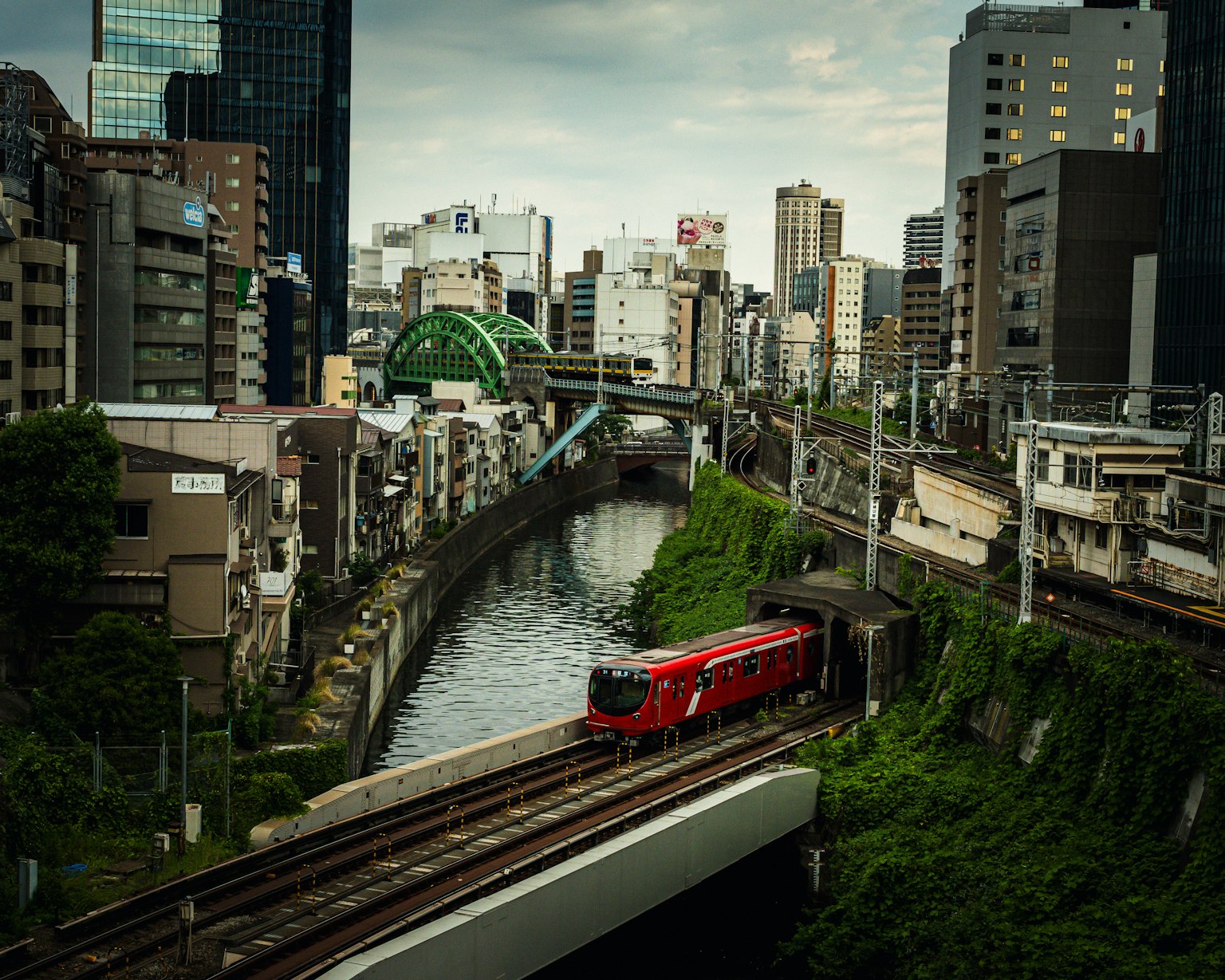 Urban landscape featuring a red train running over a waterway surrounded by greenery