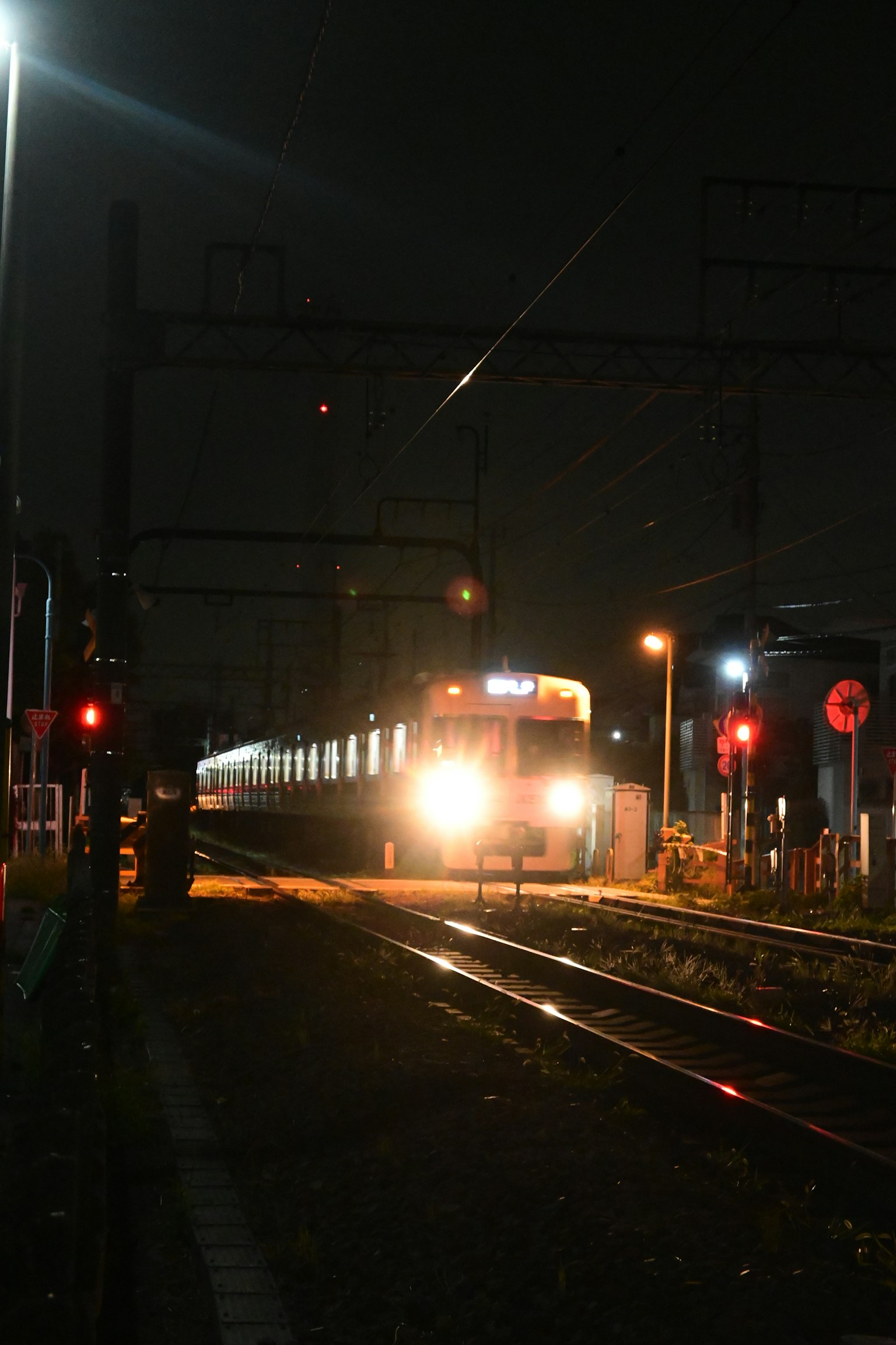 Tren llegando por la noche con faros brillantes y señales de tráfico