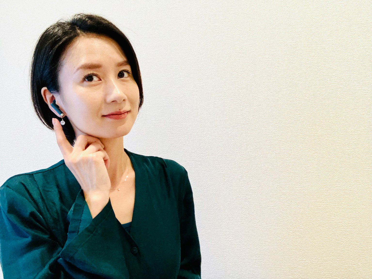 A woman smiling while wearing earbuds and pointing to them