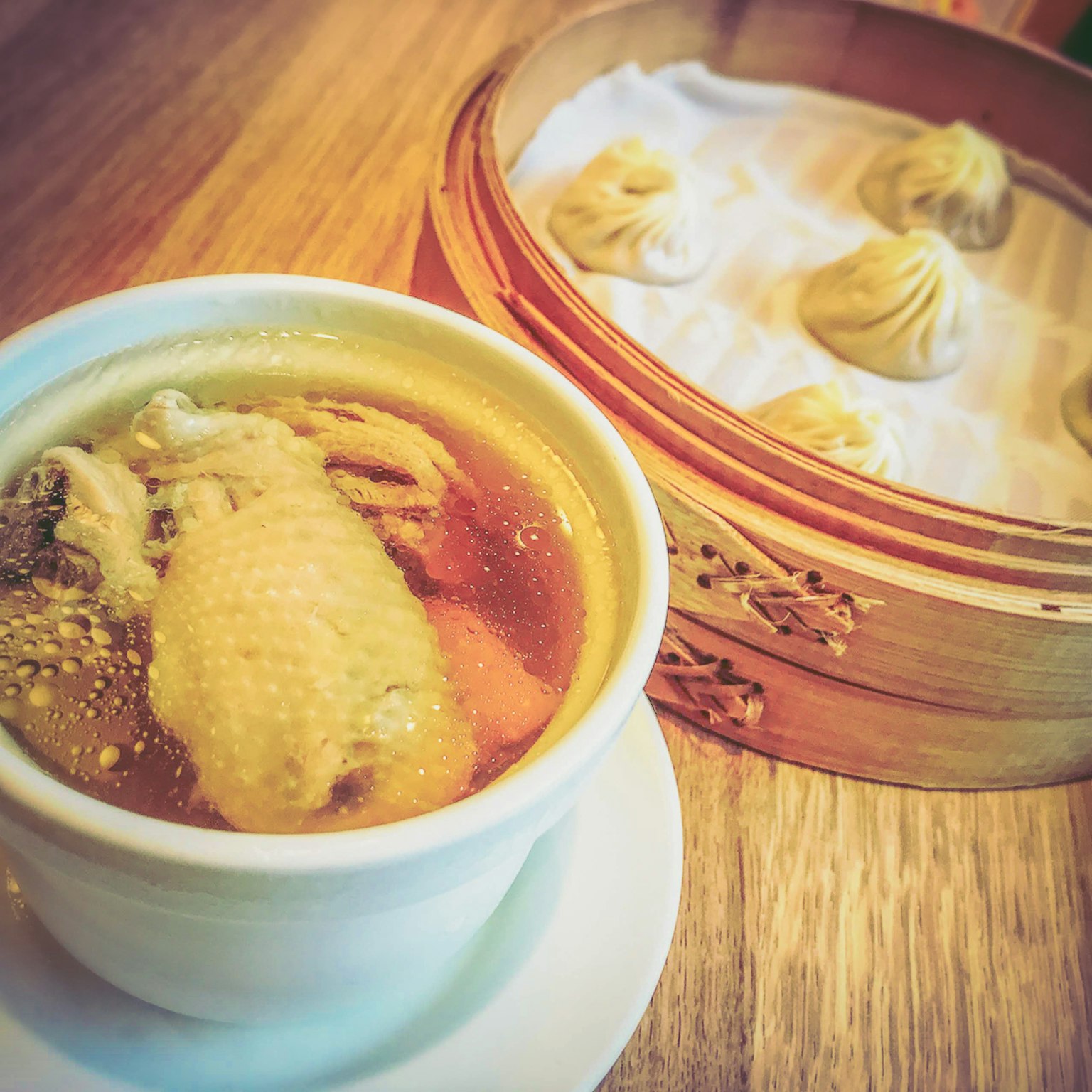 Sebuah mangkuk sup ayam dan kukusan bambu berisi dumpling di atas meja kayu