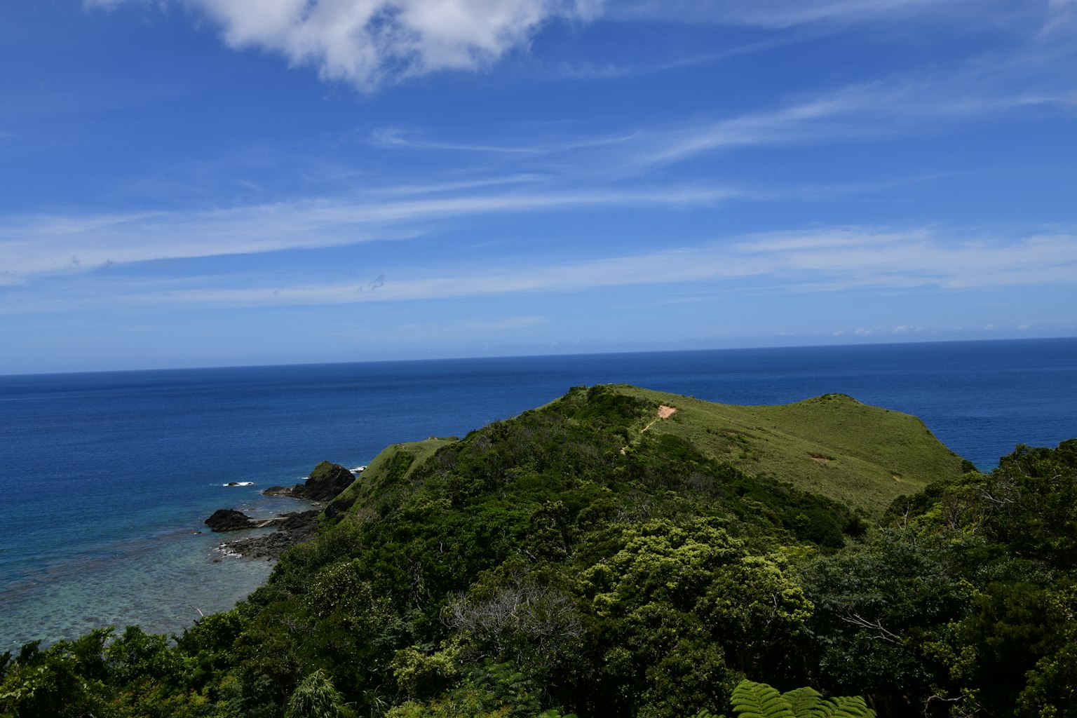 Scenic view of blue ocean and green hills with clear sky and white clouds
