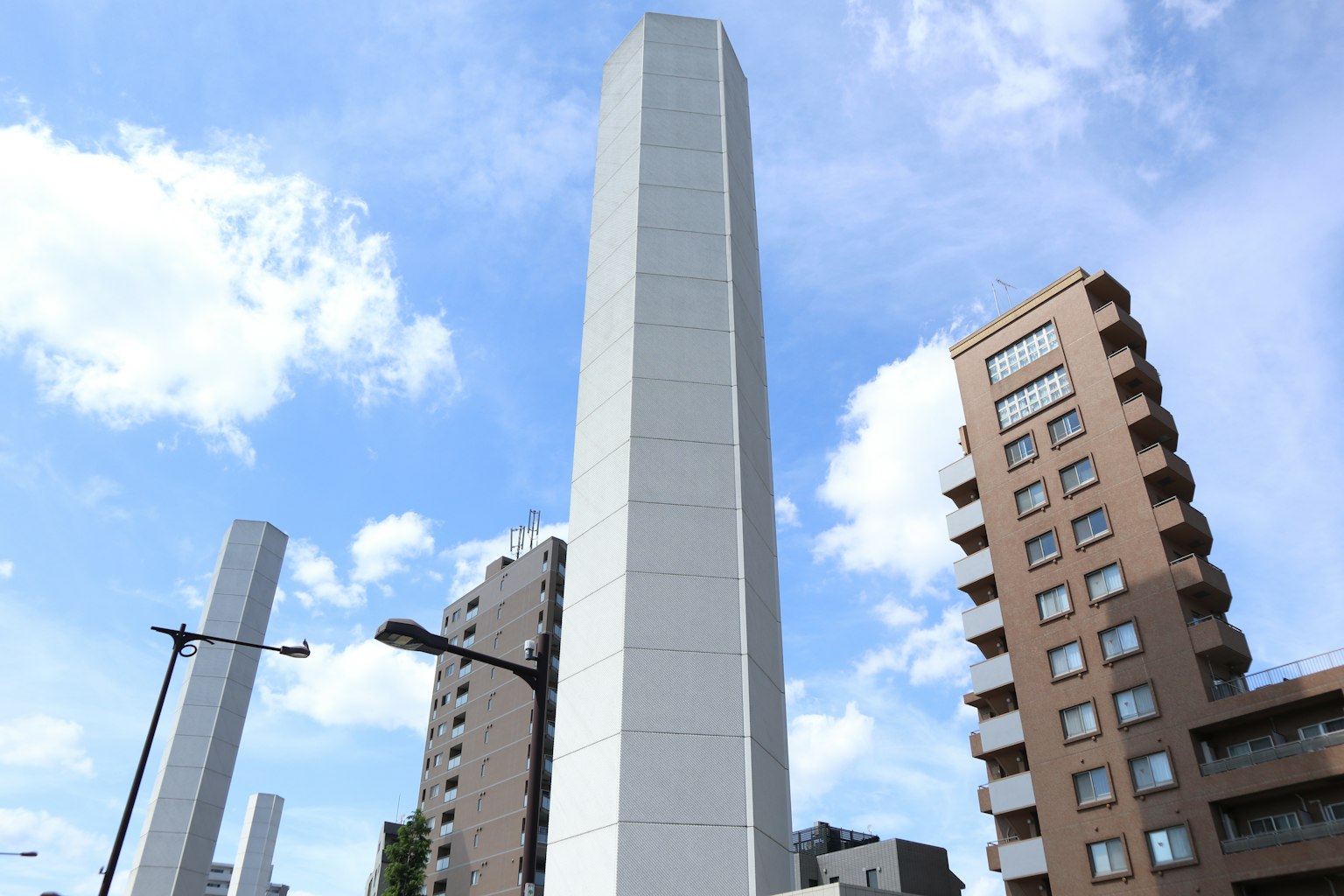 Hoher weißer Turm neben modernen Gebäuden unter blauem Himmel