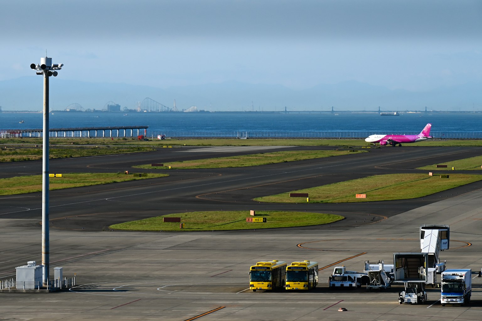 Pink airplane on runway with service vehicles at airport