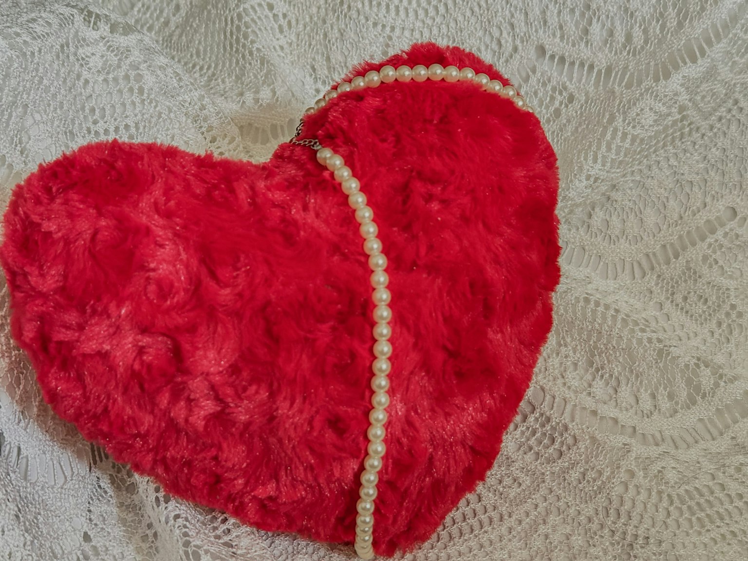 Cuscino a forma di cuore rosso con decorazione di perle su uno sfondo di pizzo