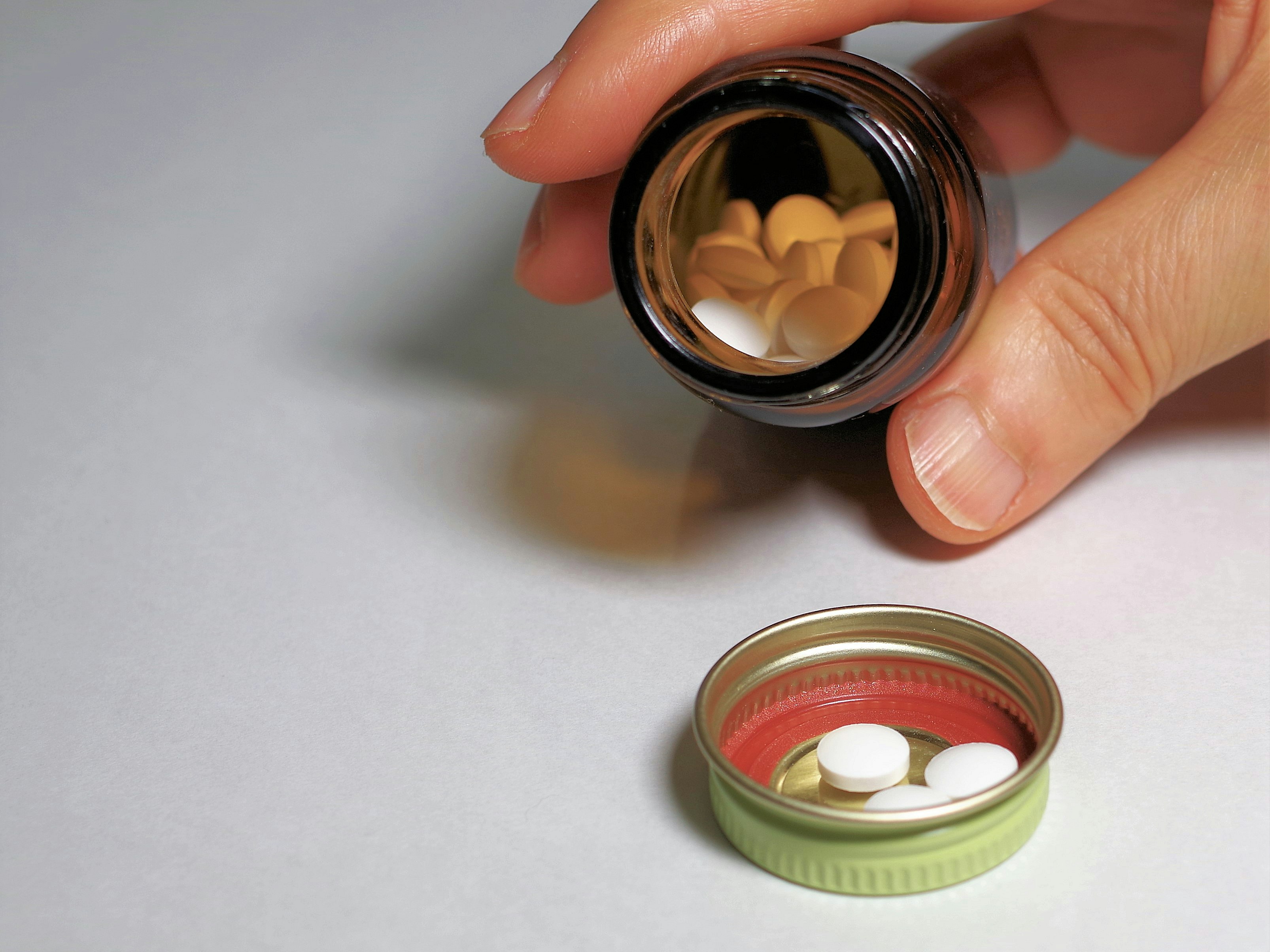 手に持った小瓶の中の錠剤と開封した薬の容器