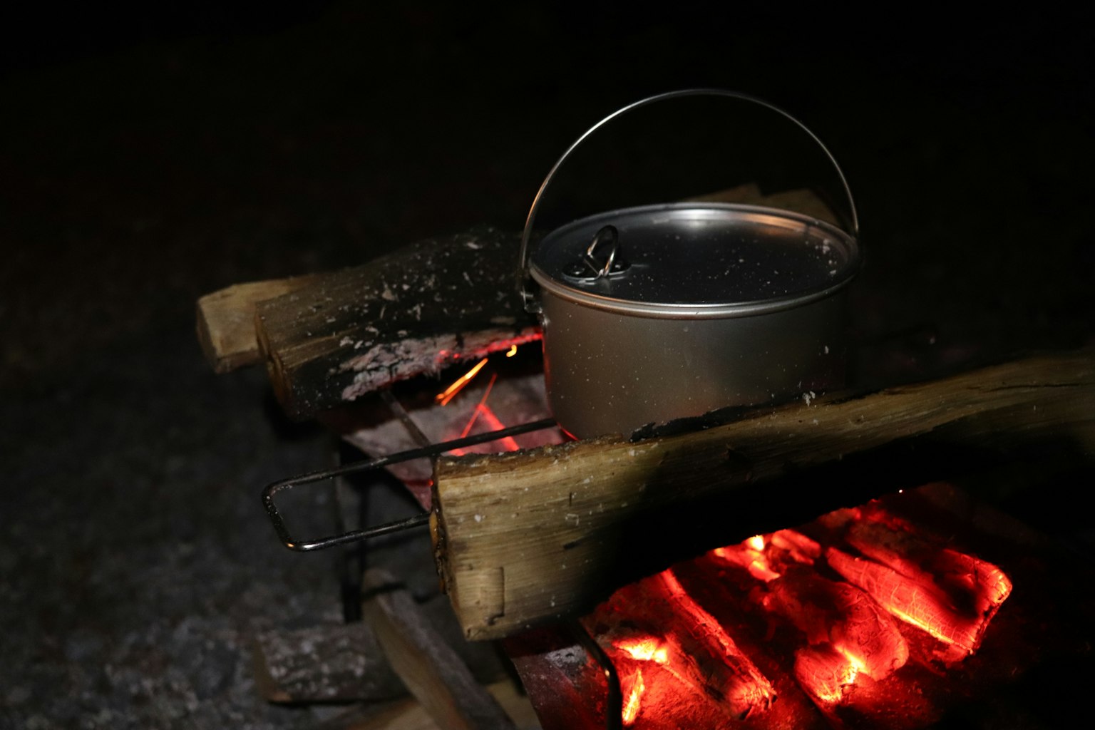 Panci logam yang diletakkan di atas api unggun di malam hari