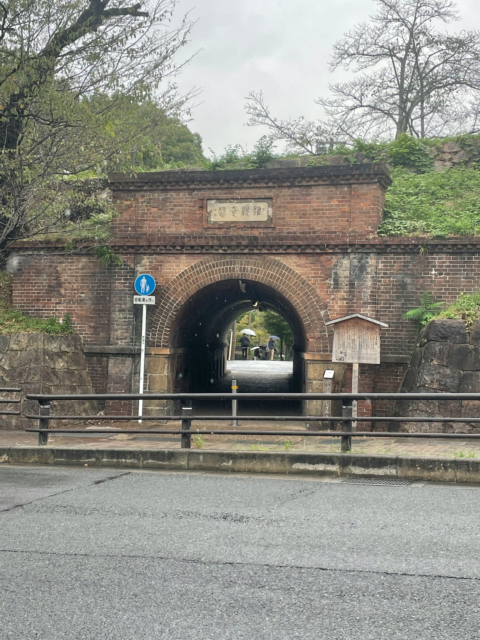 Tunnel ad arco in mattoni con un segnale stradale blu e vegetazione circostante
