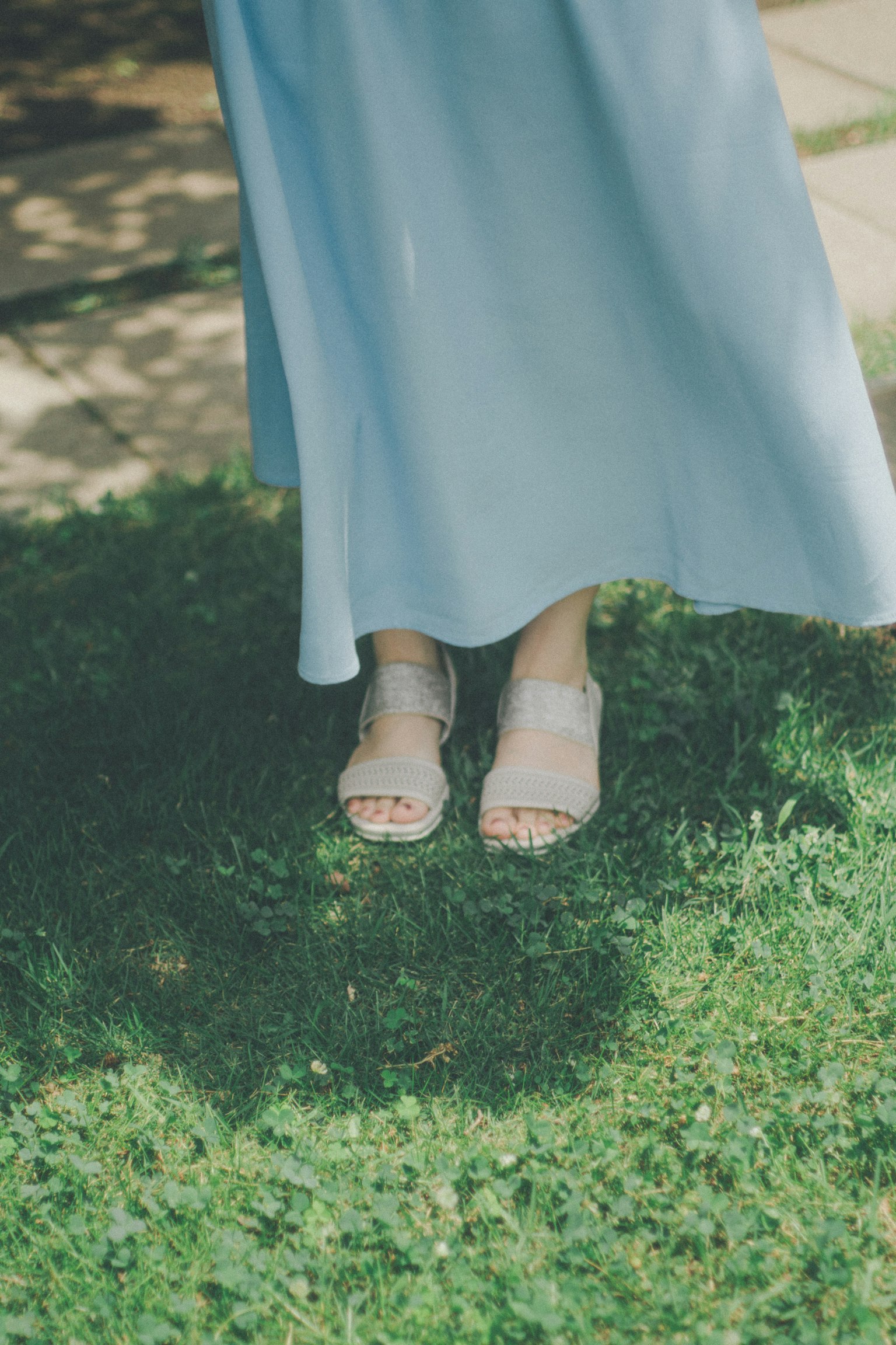 Pieds d'une femme portant une robe bleue debout sur de l'herbe verte