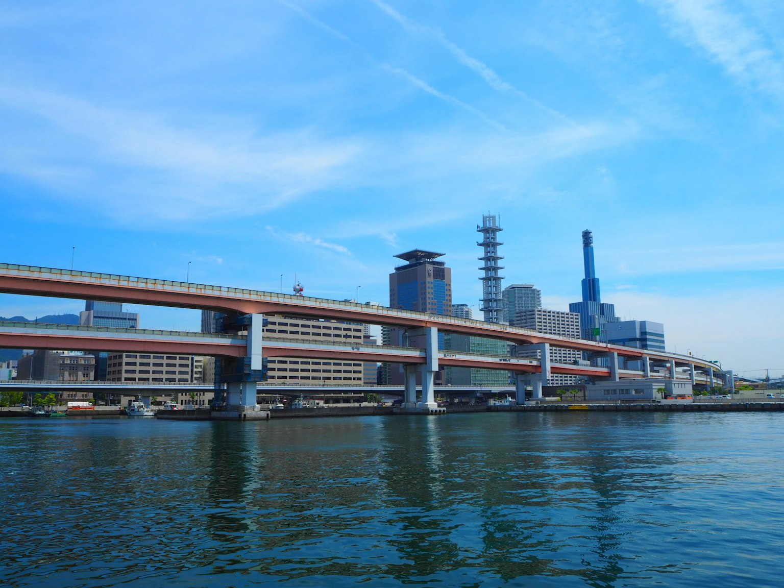 ทิวทัศน์เมืองใต้ท้องฟ้าสีฟ้าที่มีทางด่วนและอาคารสะท้อนในน้ำ