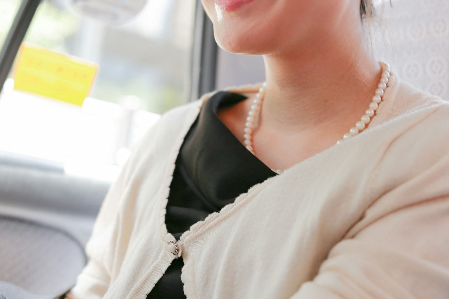 Nahaufnahme einer lächelnden Frau in einem Taxi mit schwarzer Kleidung und einer Perlenkette