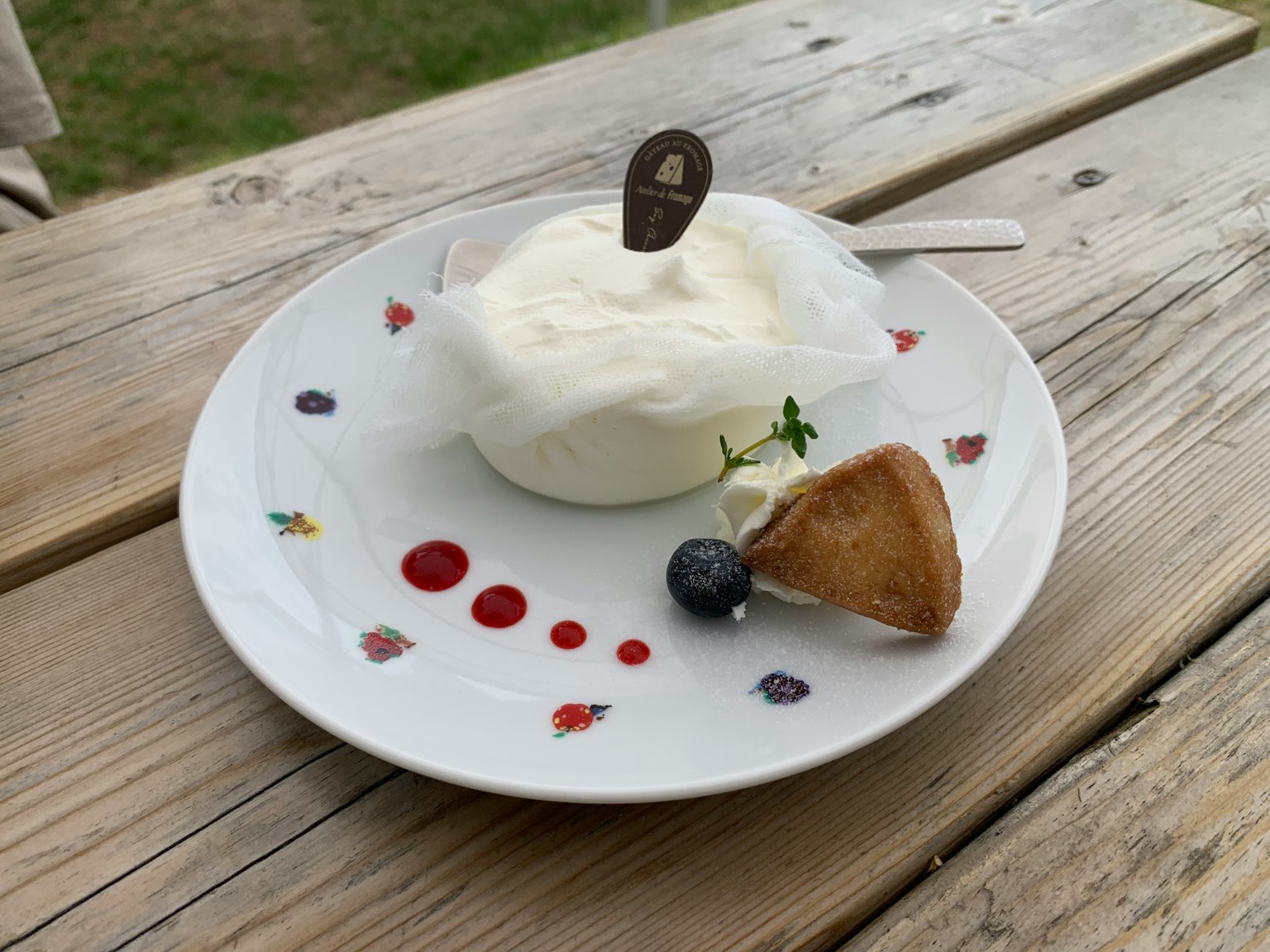 Un postre de crema blanca servido en un plato con salsa roja y un arándano como guarnición