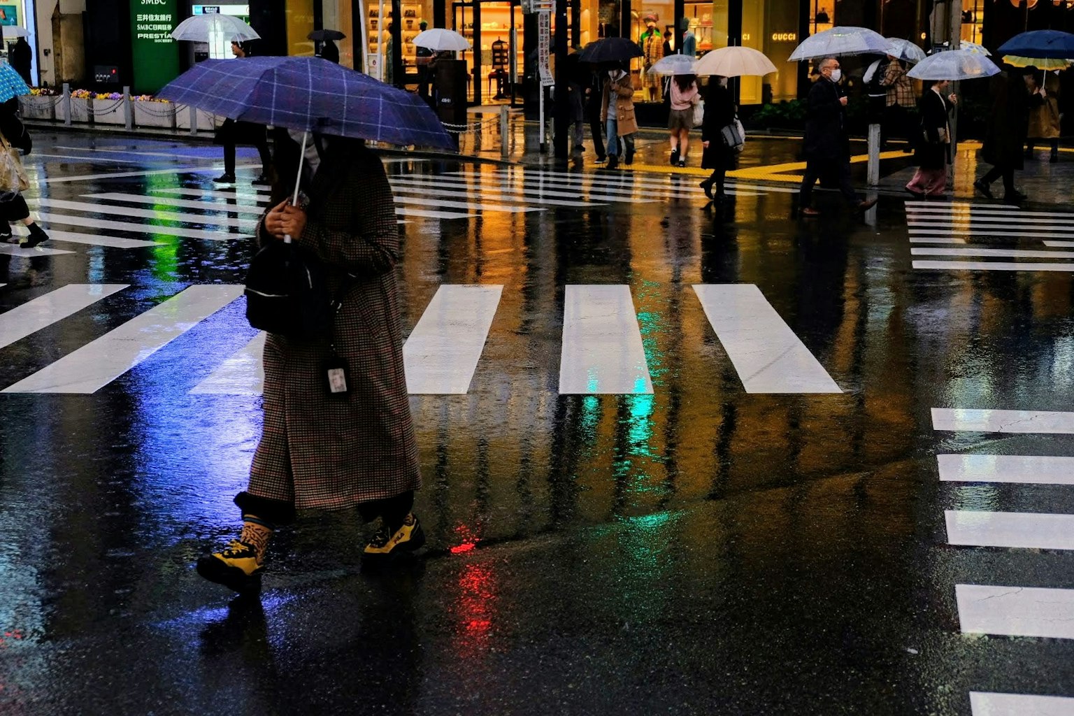 人们在雨中打着伞过马路 湿滑路面上的倒影