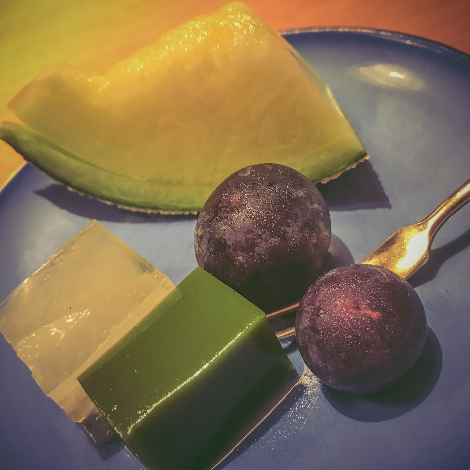 Piring berwarna-warni yang menampilkan buah dan potongan jelly termasuk melon, jelly hijau, dan anggur hitam serta biru