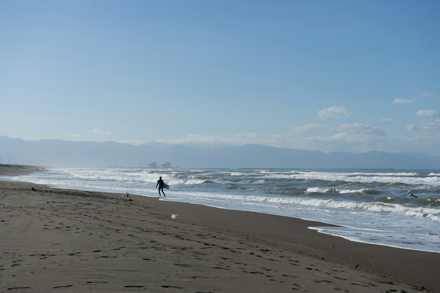 คนเดินอยู่บนชายหาดที่มีท้องฟ้าสีฟ้าและคลื่น