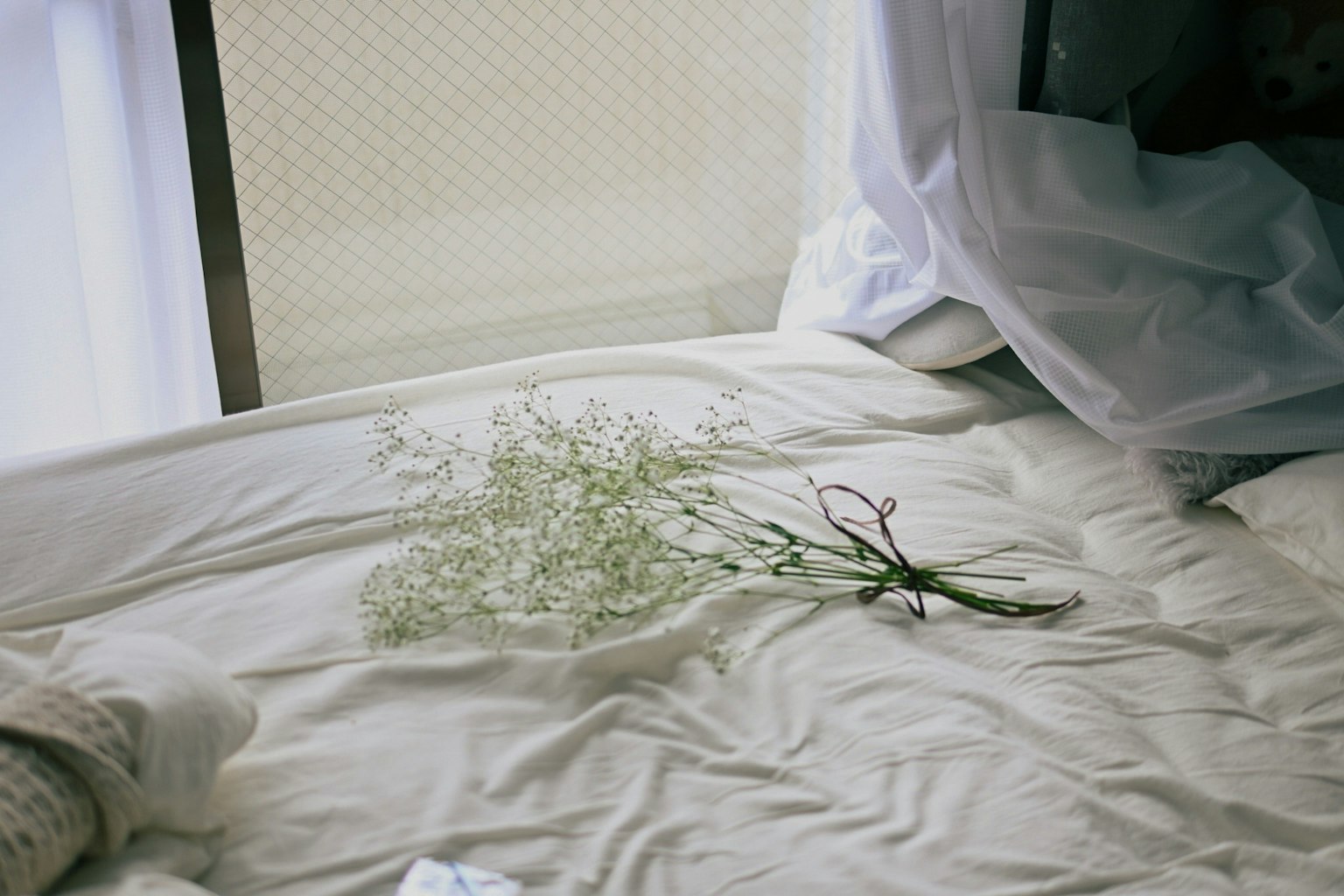 A small bouquet of flowers resting on white sheets with soft light filtering through curtains