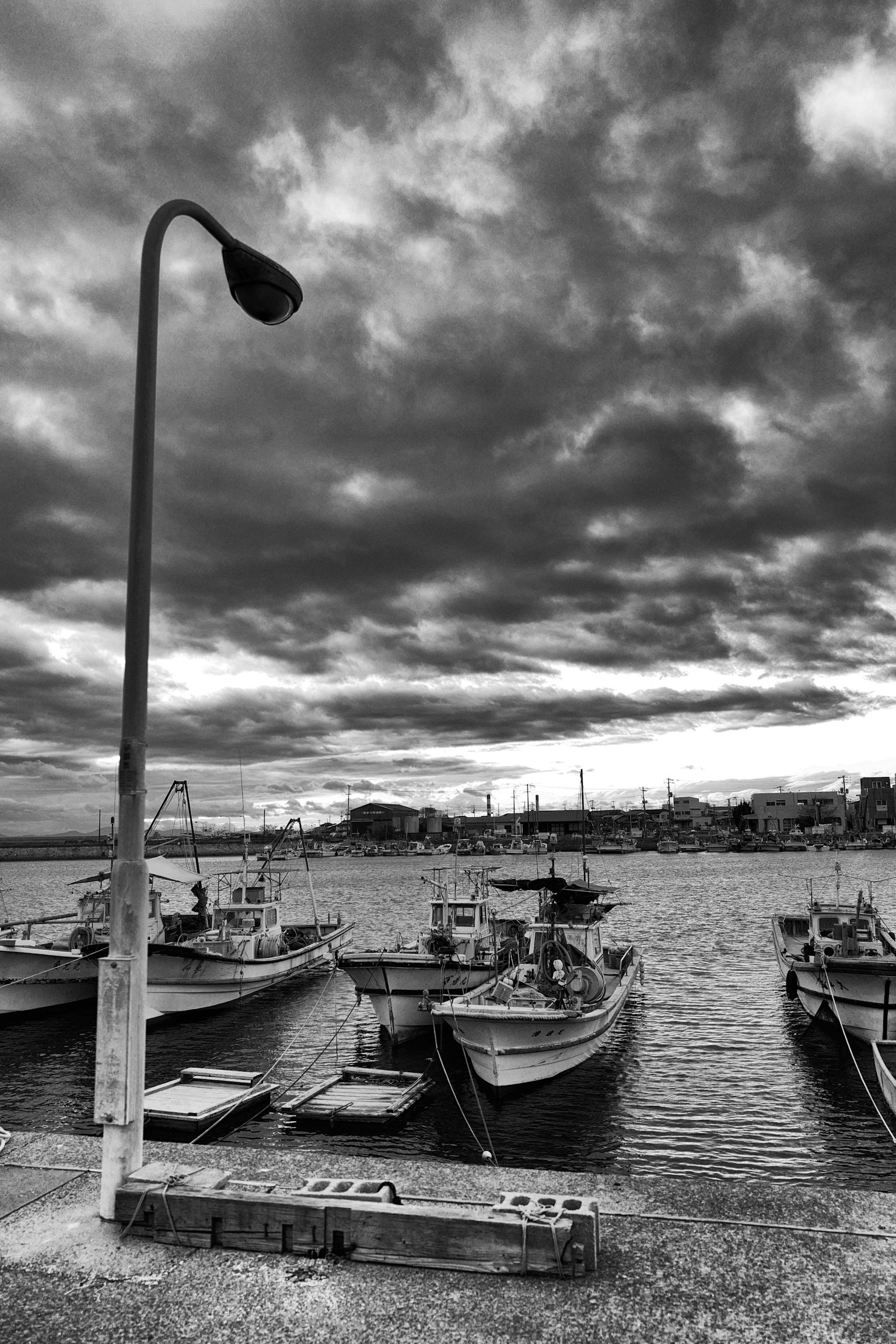 Scena di porto in bianco e nero con barche da pesca e nuvole scure