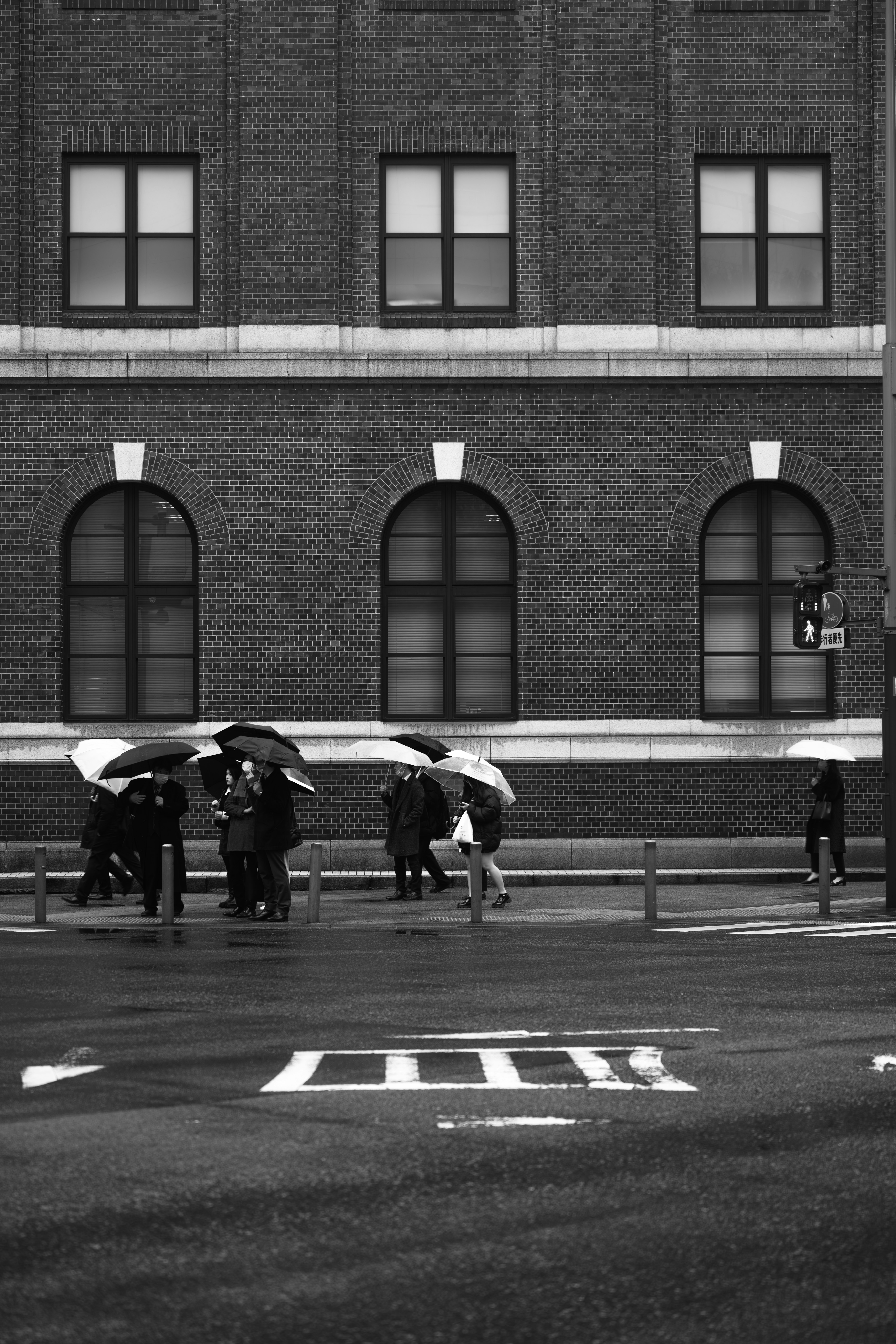 Personnes avec des parapluies à un passage piéton sous la pluie devant un bâtiment en briques