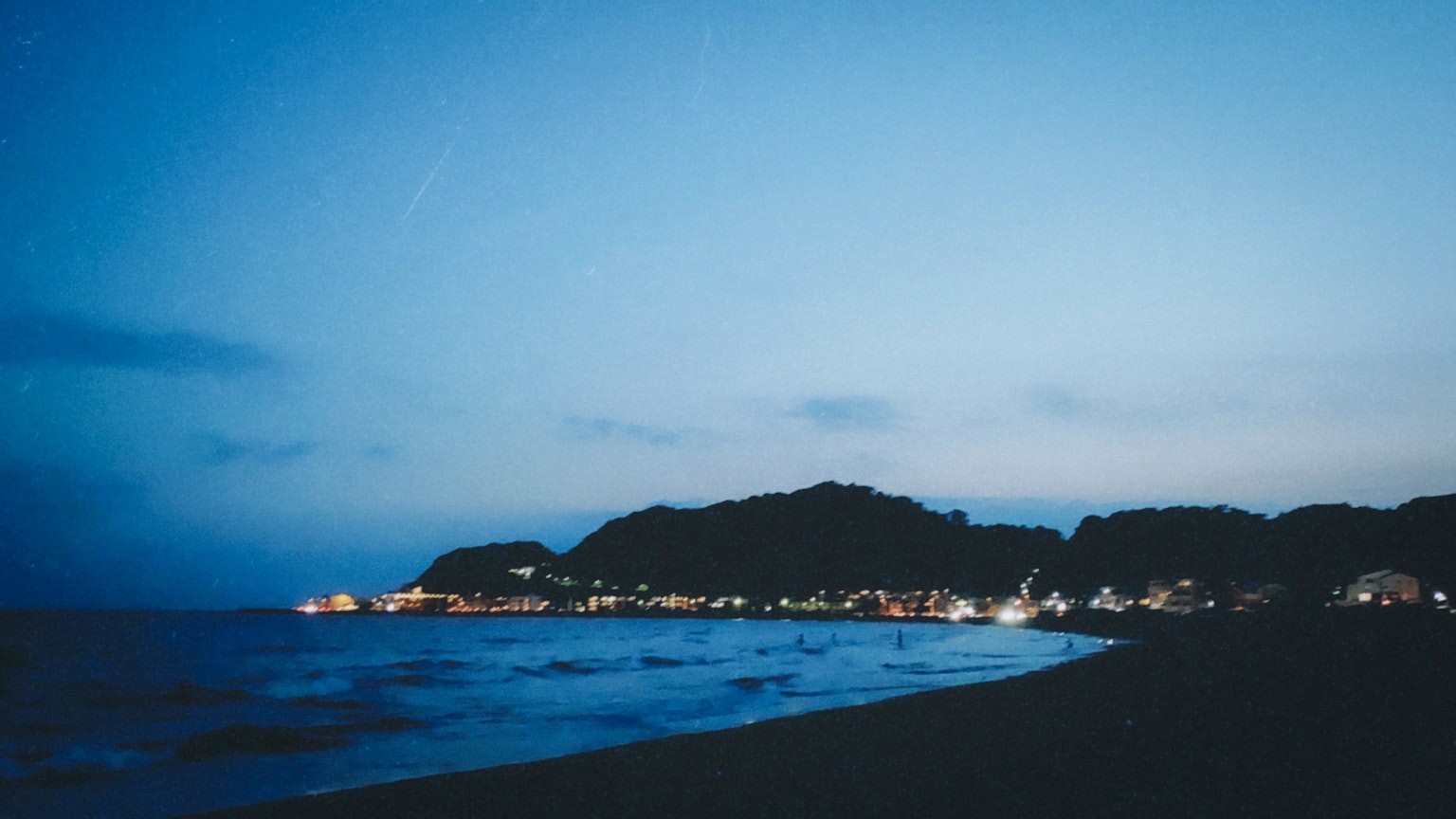 Pemandangan pantai malam dengan langit biru dan lampu jauh