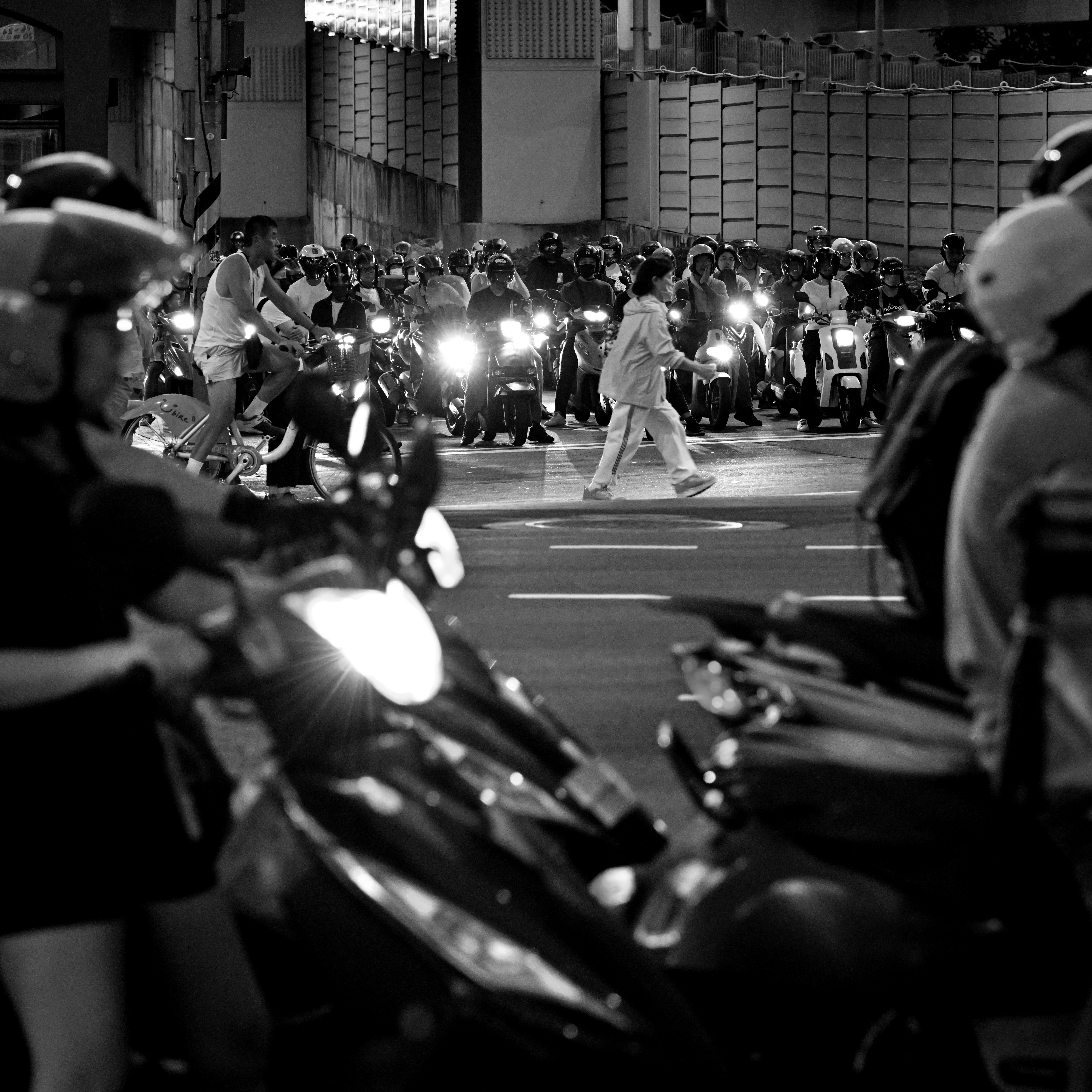 Scena notturna in bianco e nero: motociclette allineate con i fari a un incrocio
