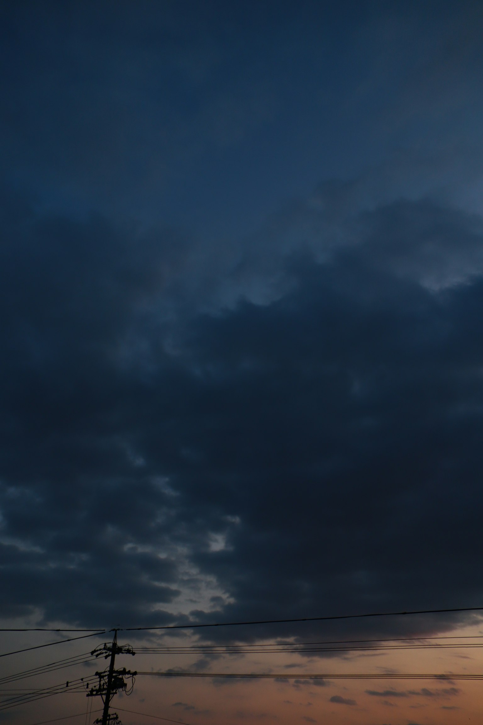 Dark clouds spread across the dusk sky with a silhouette of a power pole