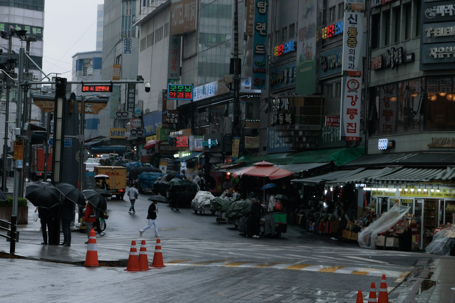 Cảnh đô thị trong mưa có người cầm ô và các cửa hàng