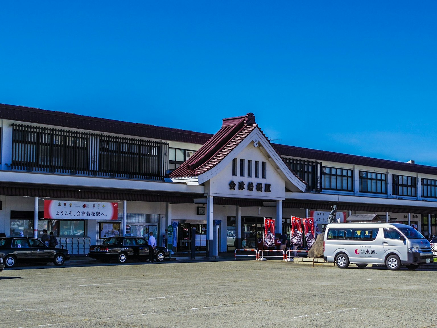 Traditionelles japanisches Bahnhofsgebäude unter einem klaren blauen Himmel mit umliegenden Fahrzeugen